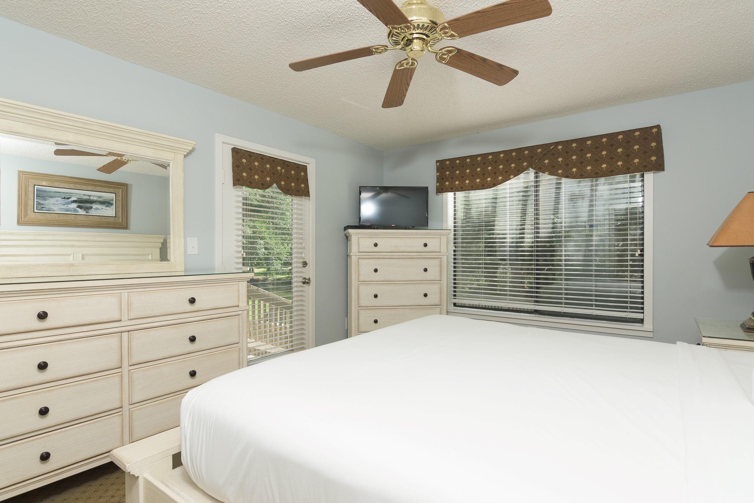 Bedroom with a white bed, light wood dressers, and a ceiling fan.