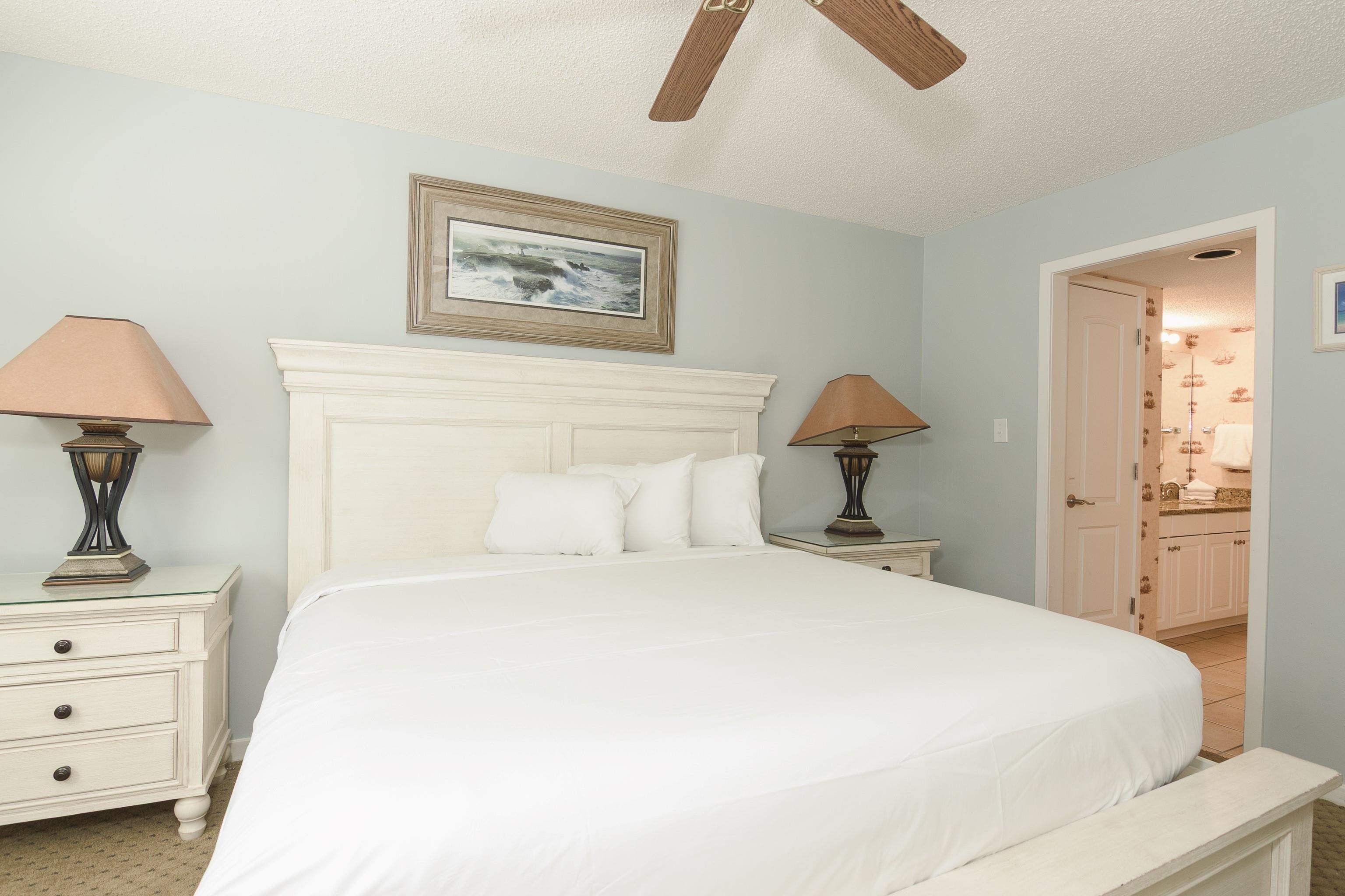 Bedroom with a large white bed, matching bedside lamps, and an open doorway to the bathroom.