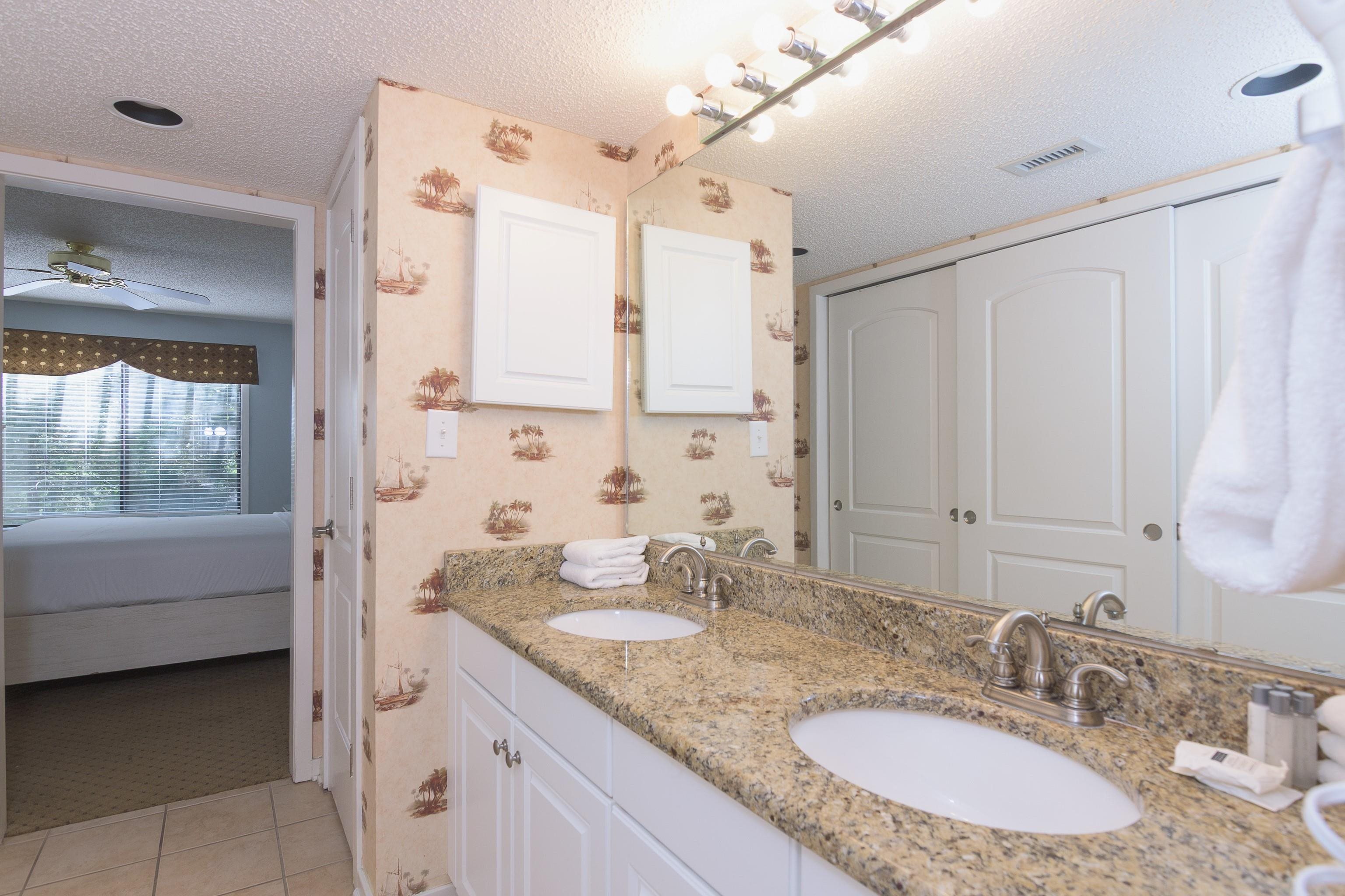 Bathroom vanity with two sinks and granite countertop; an open doorway looks into a bedroom.