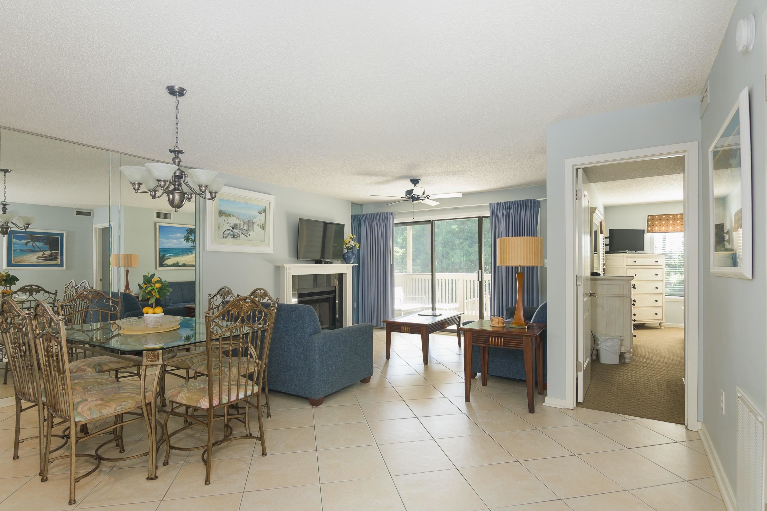 Open-plan living and dining room with mirrored walls, a fireplace, blue seating, and sliding doors to a balcony.