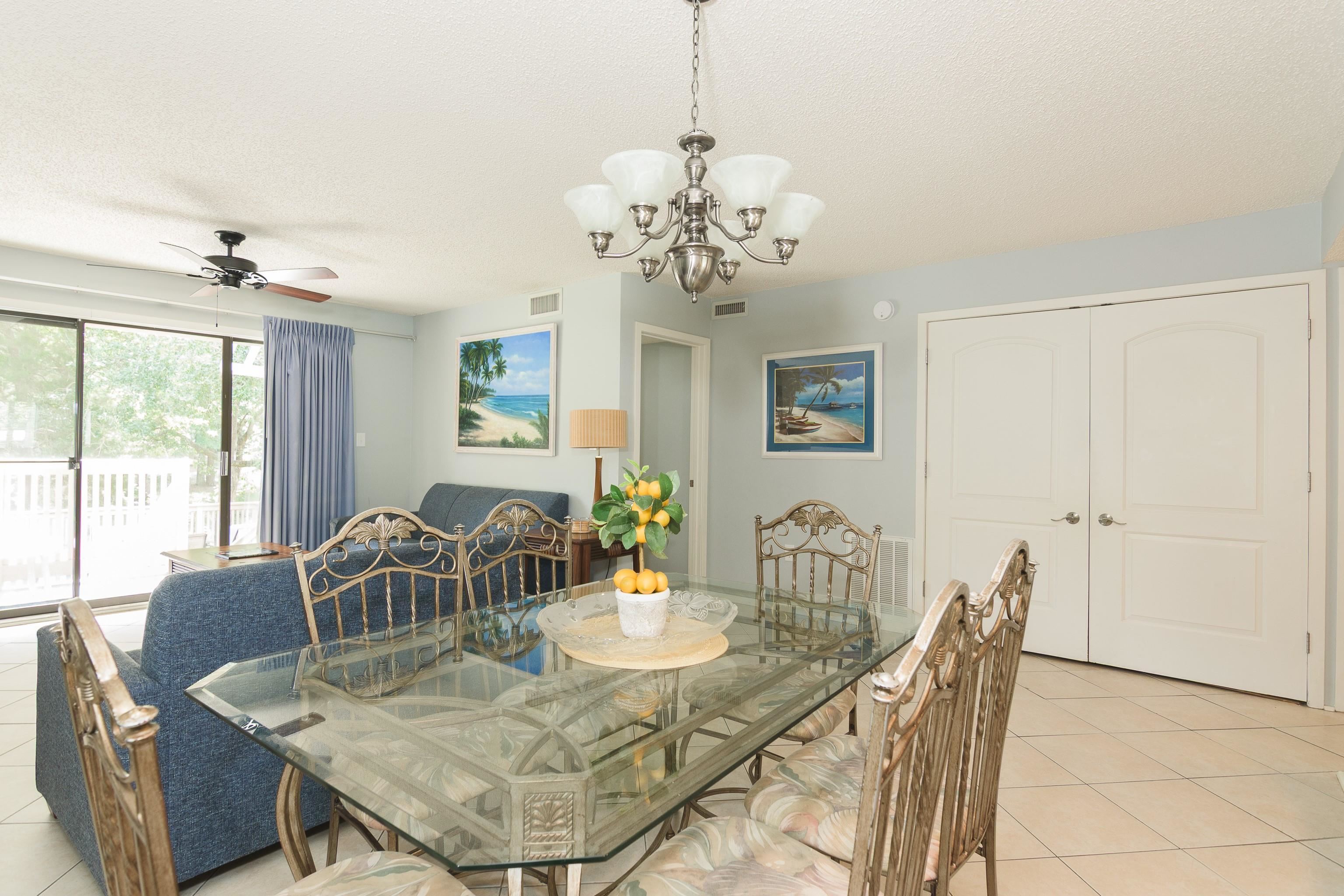 Dining area with a glass-top table and ornate chairs beside a blue sofa and sliding doors to a deck.