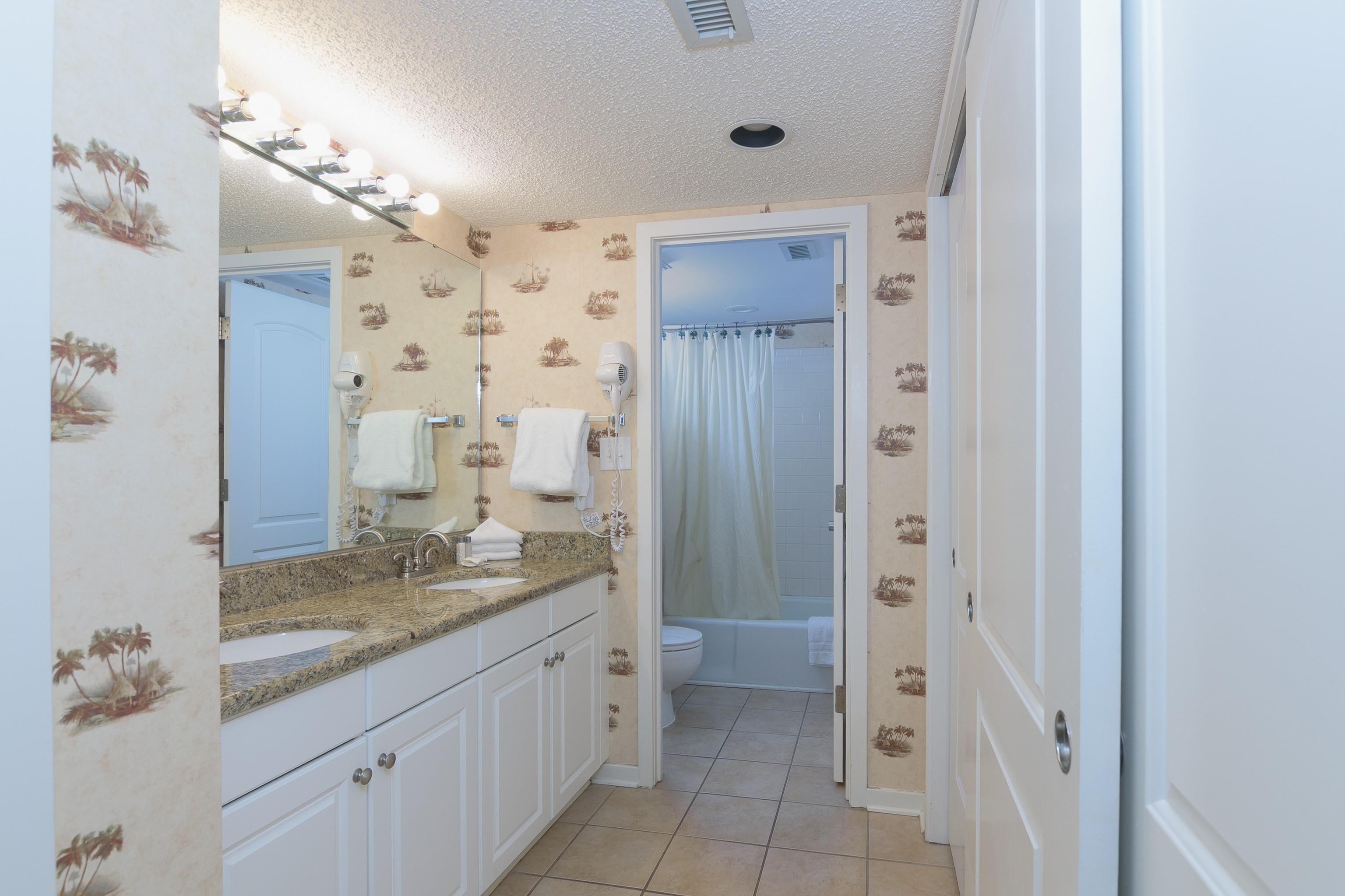 Bathroom with a granite double vanity, large mirror, and shower-tub area.