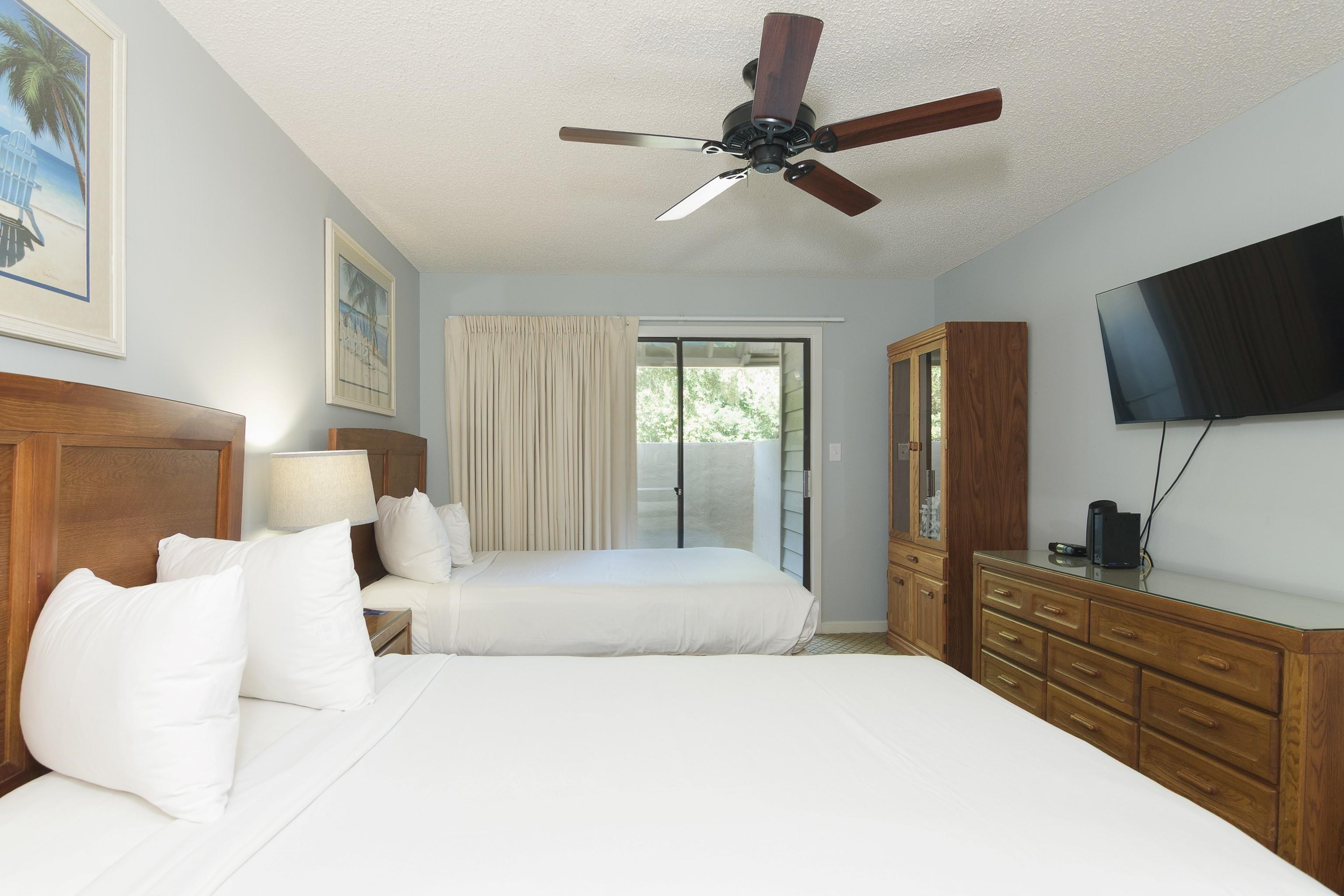 Bedroom with two white beds, wooden furniture, and sliding glass doors to a balcony.