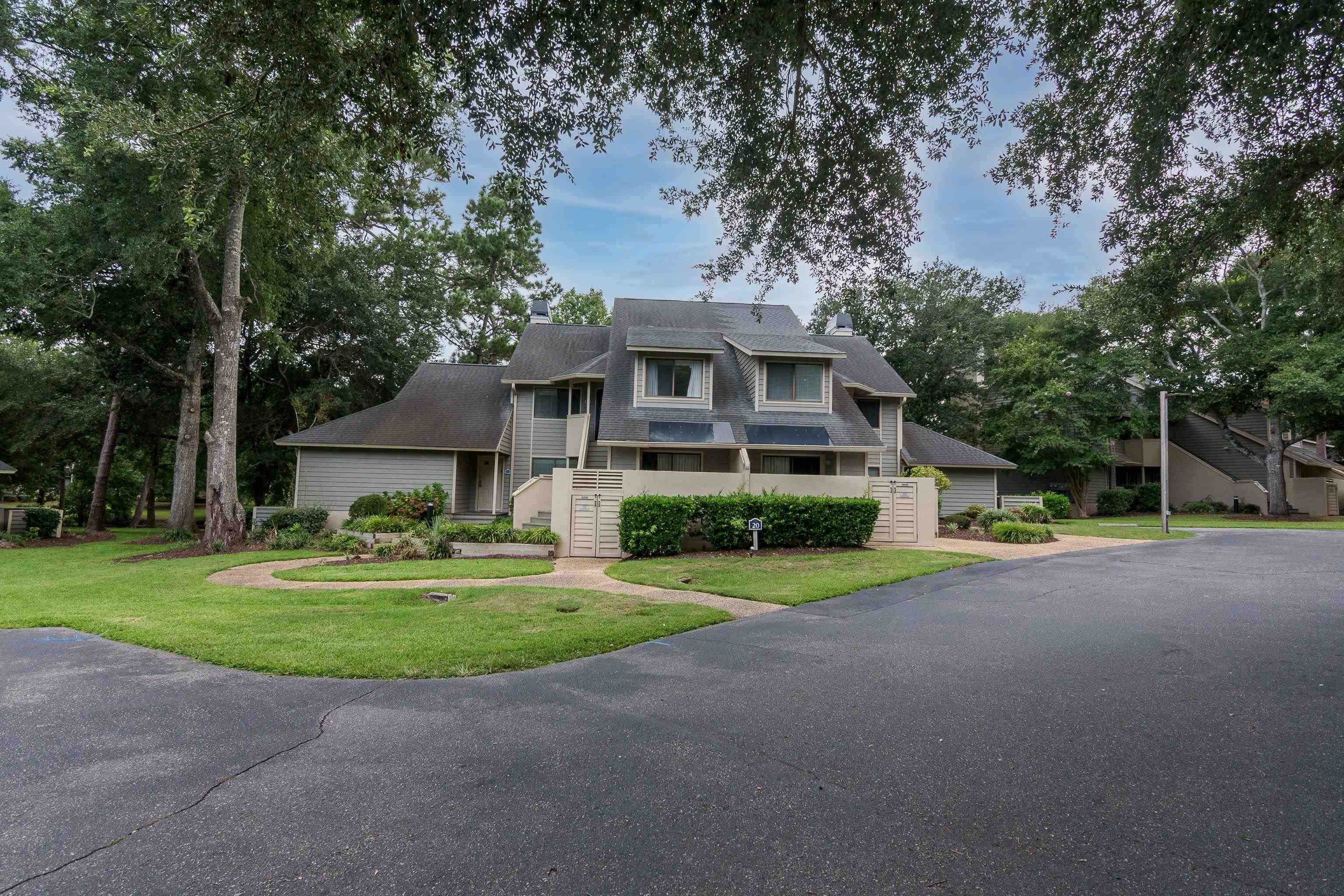 Gray multi-level condominium with dormer windows, solar panels, and a fenced patio.