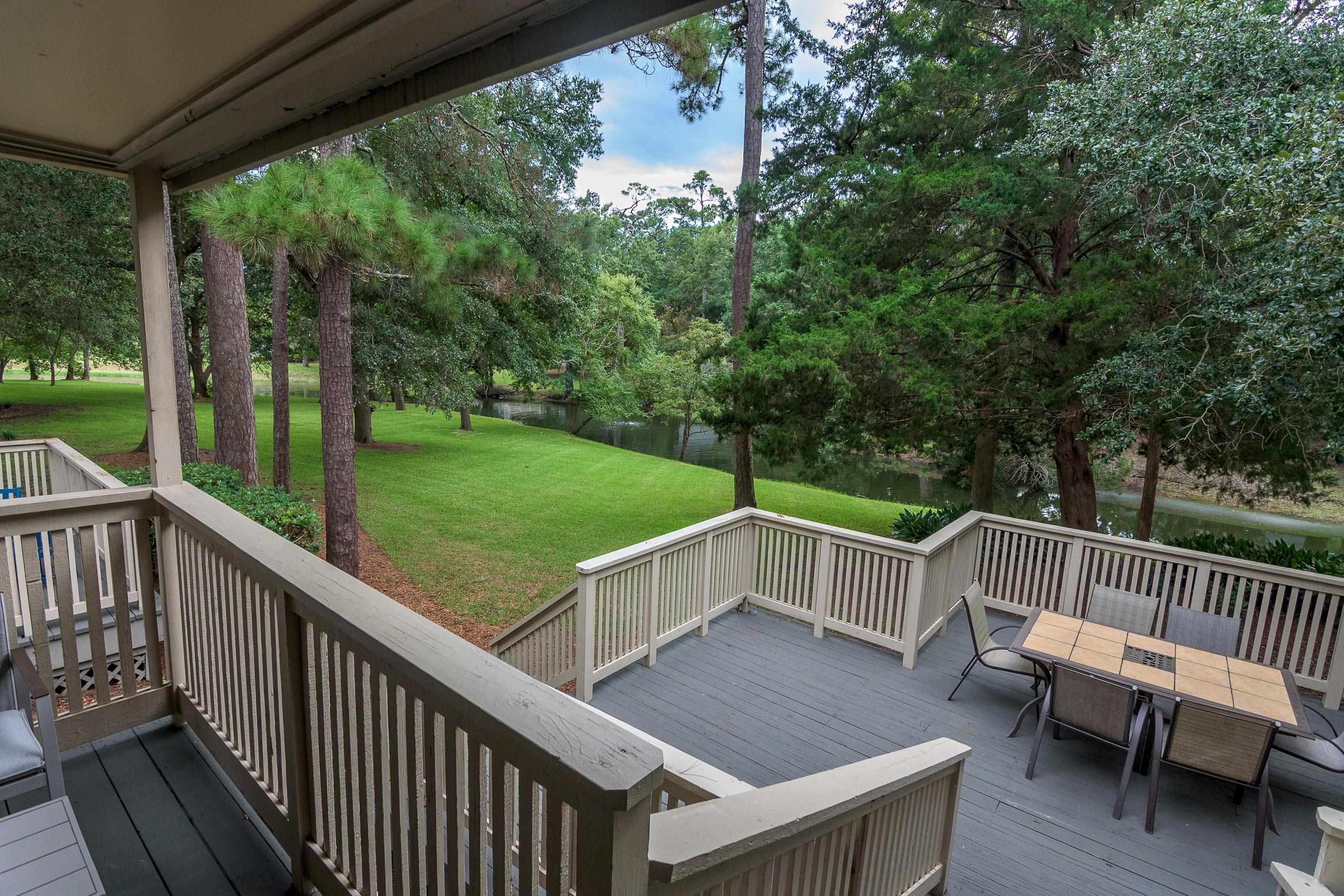 Covered deck with outdoor dining set overlooking a tree-lined waterway and lawn.