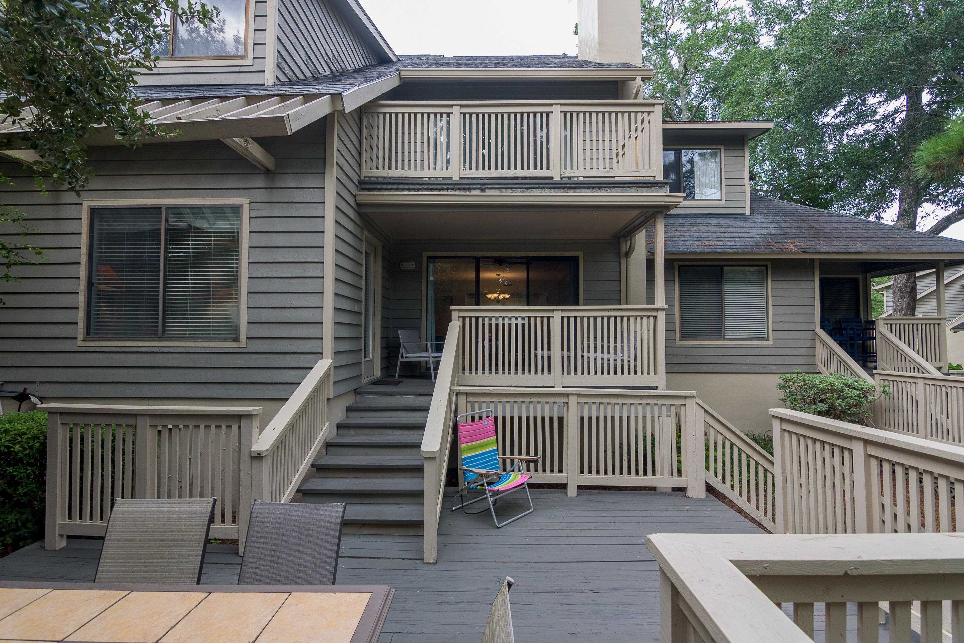 Townhouse exterior with a raised deck, multiple balconies, stairs, and colorful folding chair.