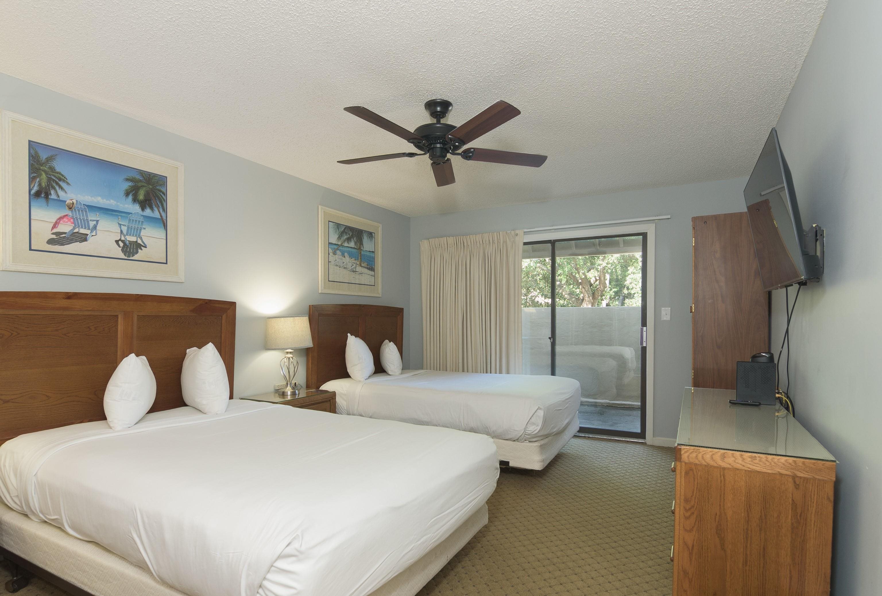 Bedroom with two beds, dark wood headboards, and sliding glass doors to a patio.