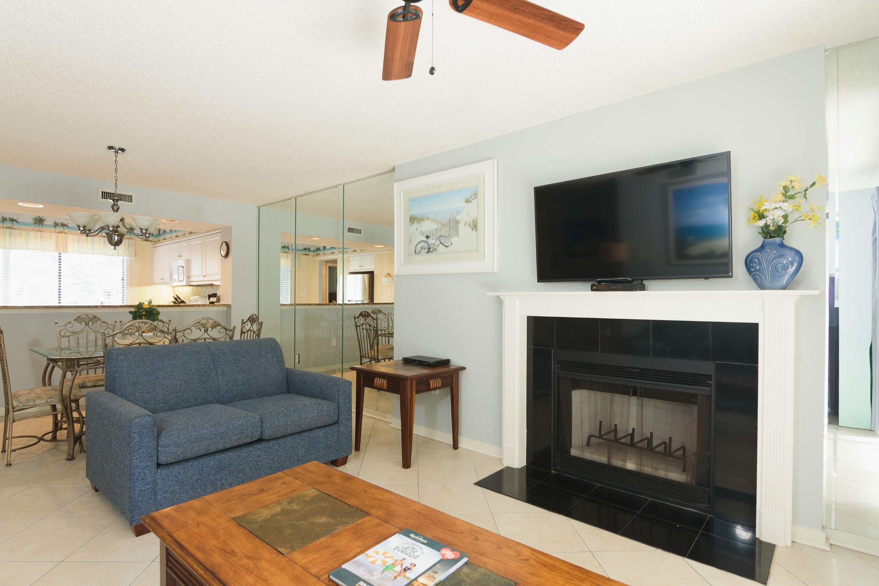 Furnished living room with a blue sofa, black-tile fireplace, and mirrored wall overlooking the dining area.