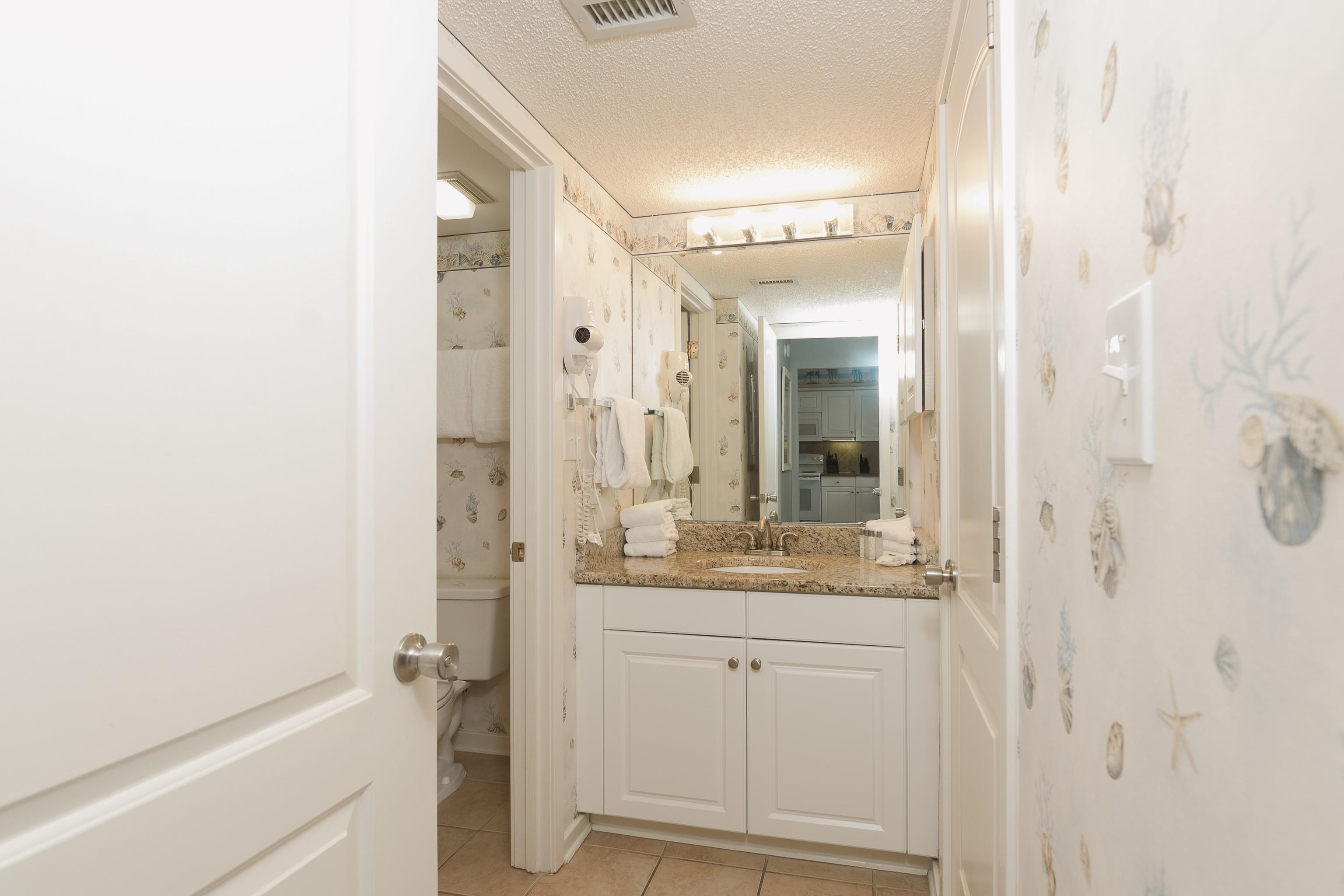 Bathroom vanity with a granite countertop, white cabinets, and seashell-patterned wallpaper.