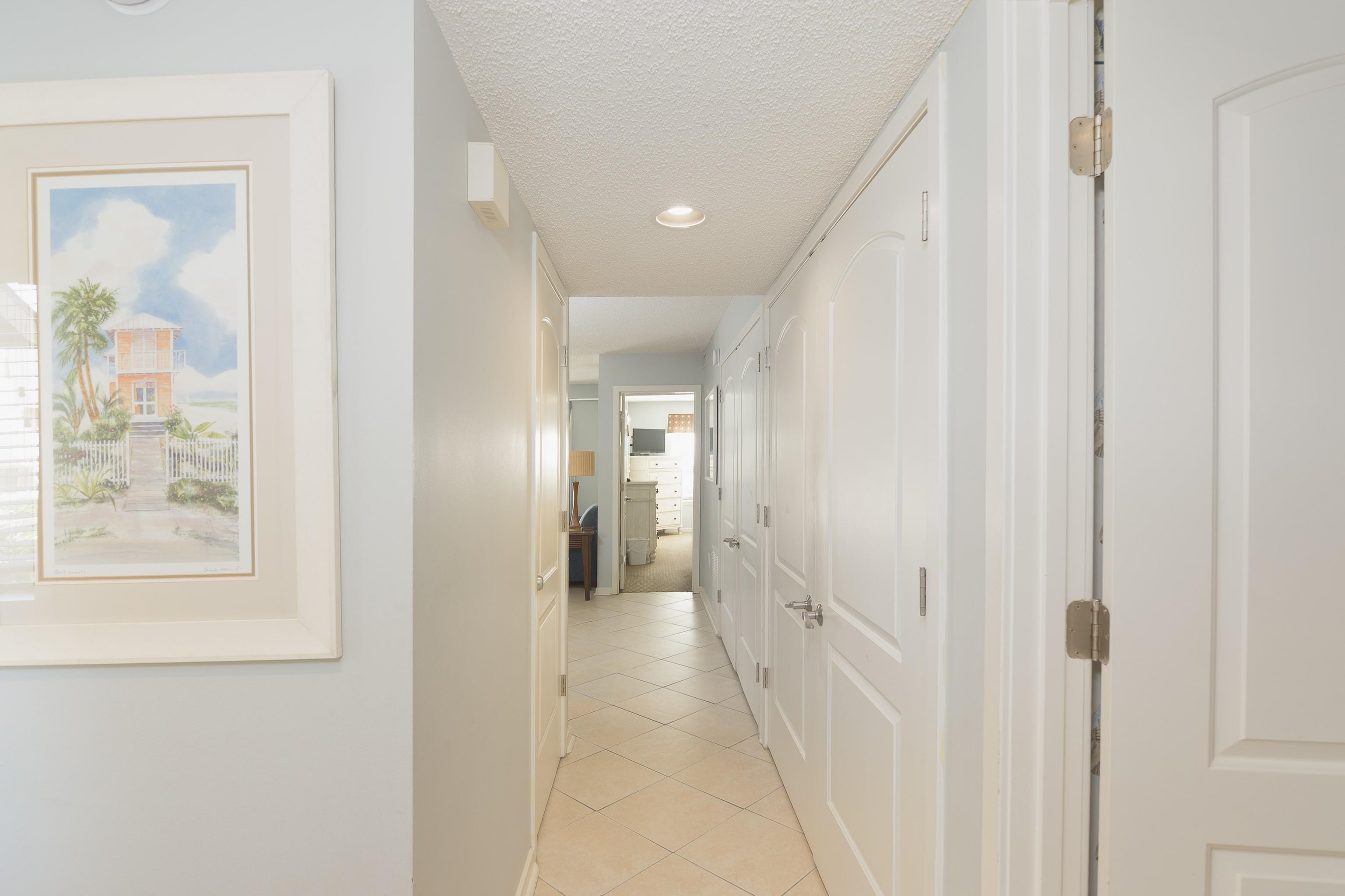 Tiled hallway lined with white paneled doors, leading toward a room with a dresser.