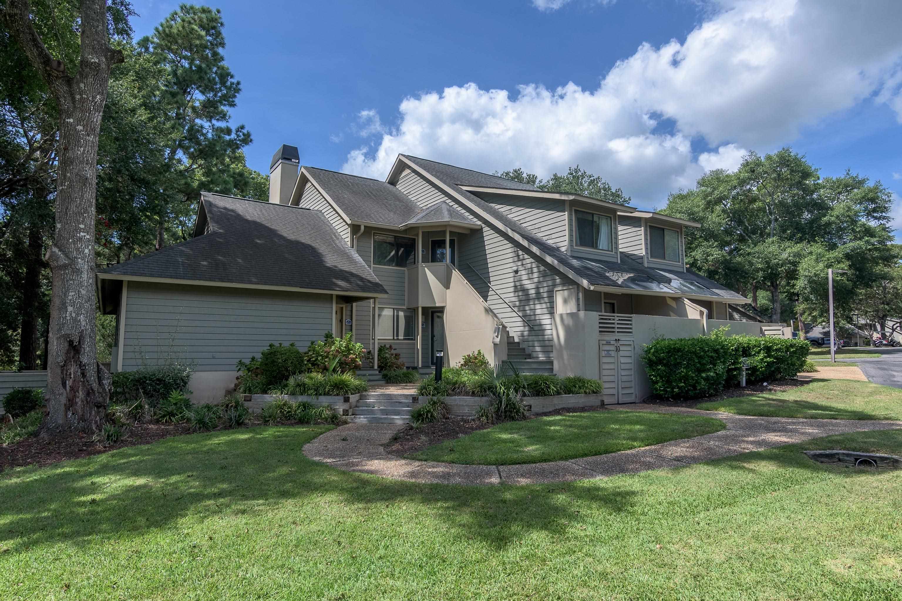 Gray-sided multi-unit residence with gabled roofs, an exterior staircase, and a landscaped front lawn.