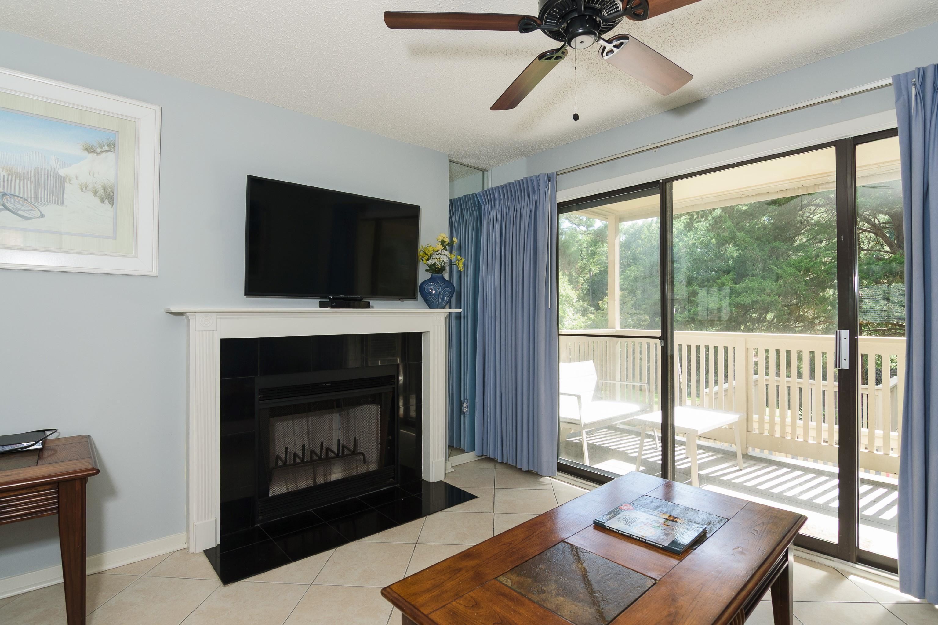 Living room with a fireplace and sliding doors to a balcony overlooking trees.