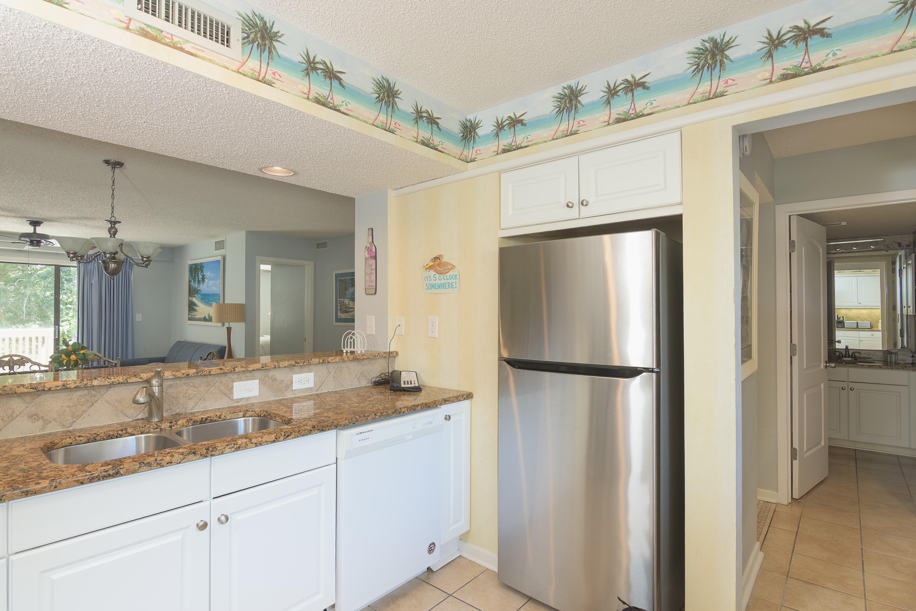 Kitchen with white cabinets, granite counters, stainless-steel refrigerator, and tropical palm-tree ceiling border.