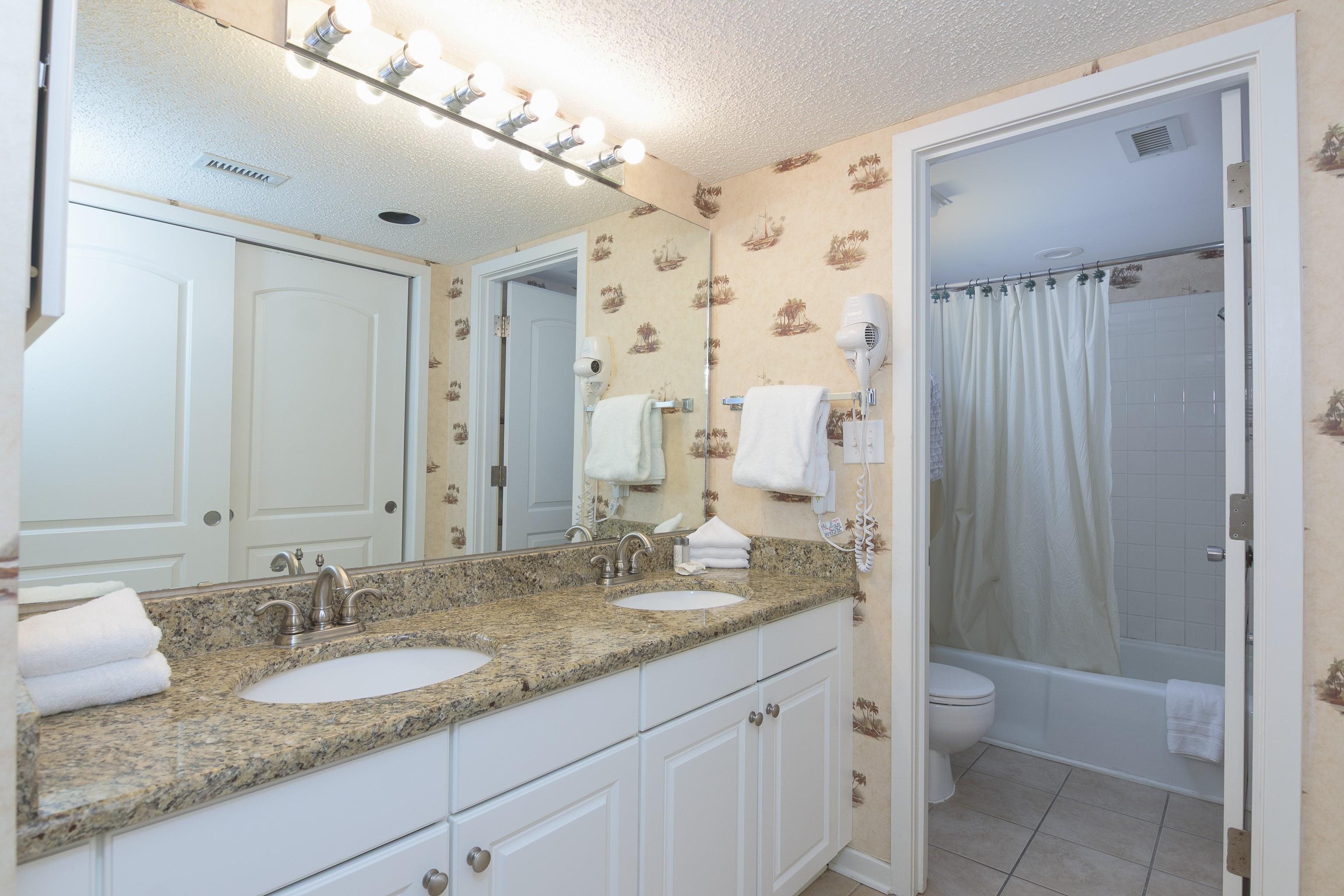 Bathroom with a double vanity and granite countertop beside a tub and shower.