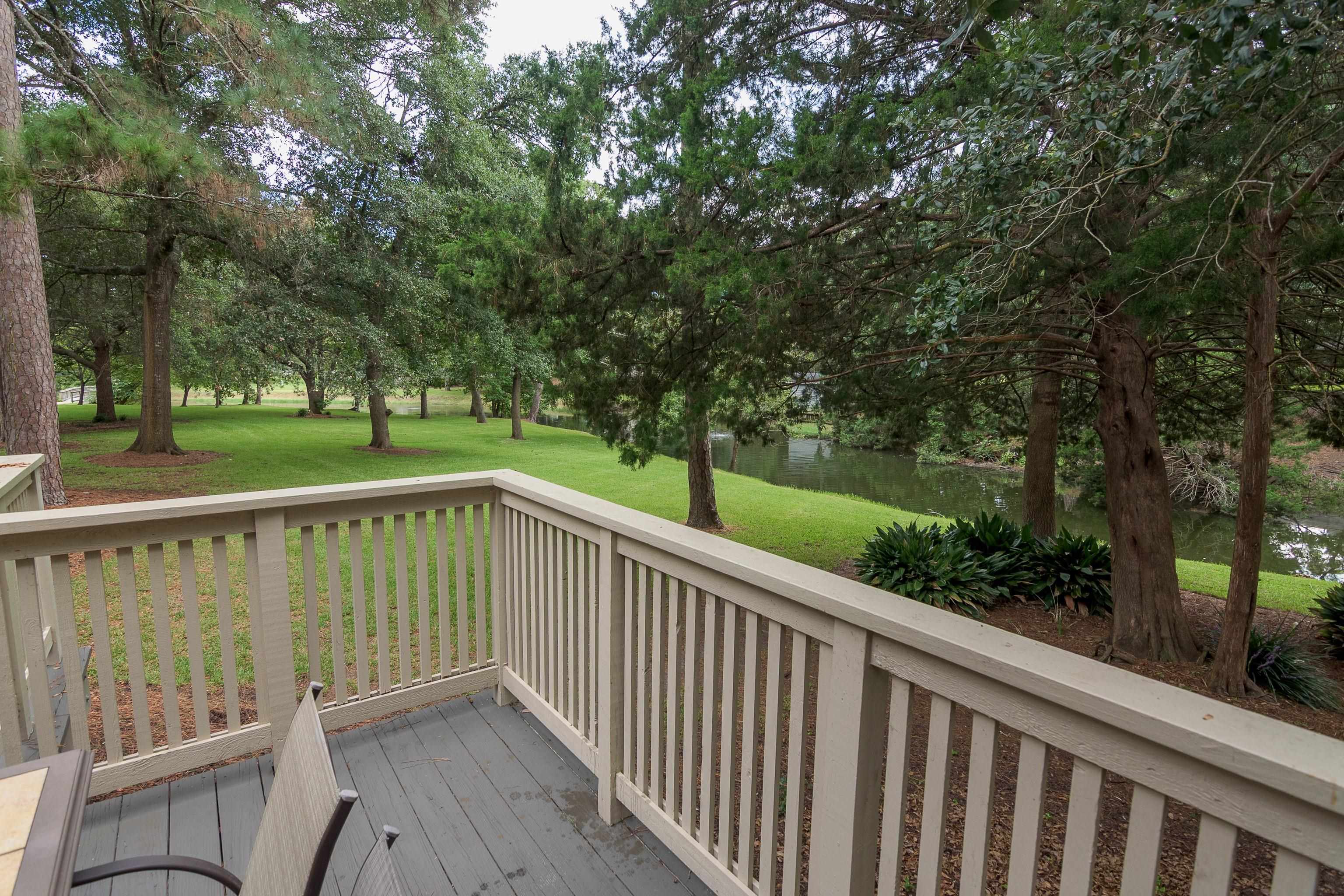 Deck overlooking a tree-lined creek, with gray flooring, cream railings, and patio chairs.