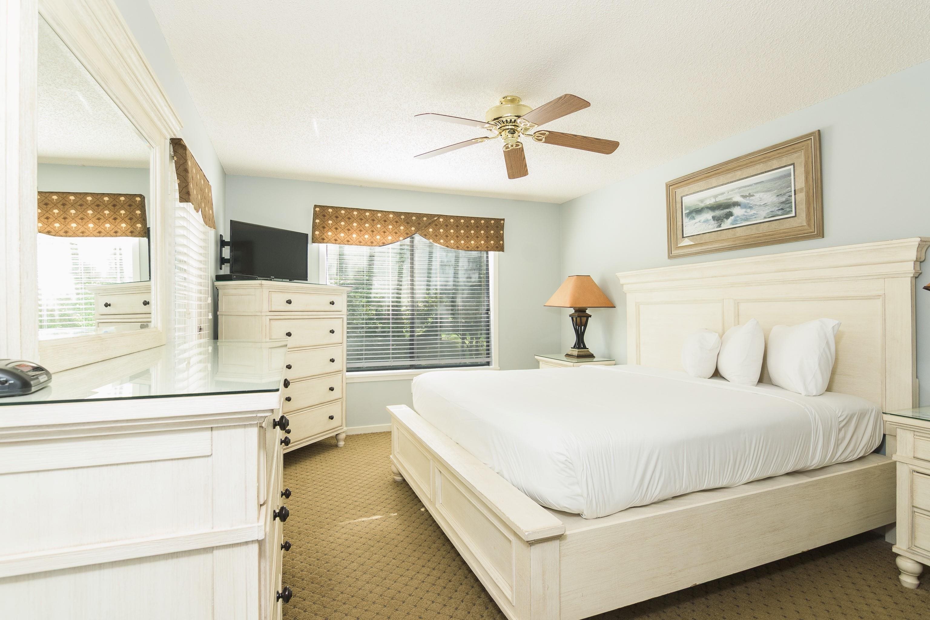 Bedroom with a large white bed, matching cream furniture, and framed ocean artwork above the headboard.