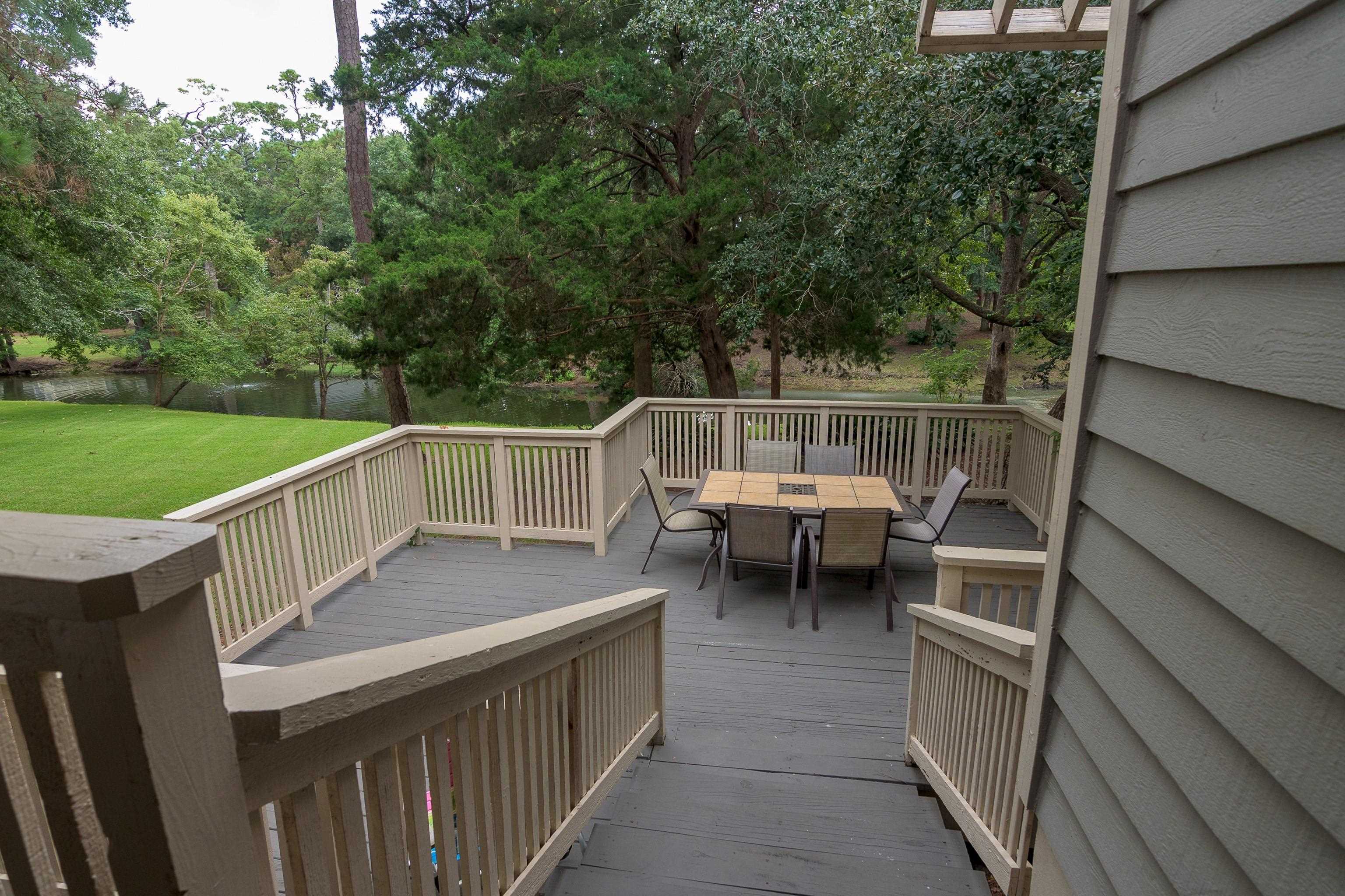 Wooden deck with a dining set overlooking a pond and wooded lawn.