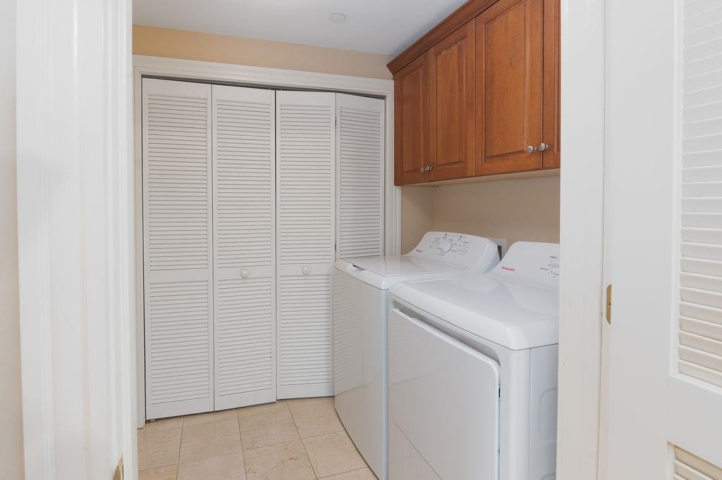 Laundry room with a white washer and dryer, wood cabinets, and louvered closet doors.