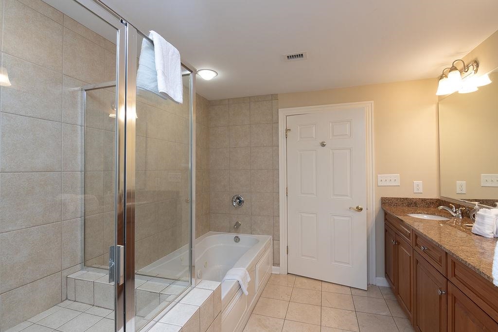 Bathroom with a glass shower, bathtub, and wood vanity topped with granite.