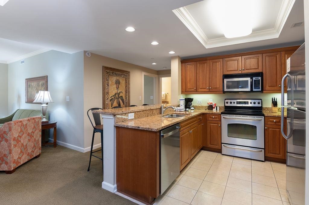 Furnished kitchen with wood cabinets, granite counters, and stainless steel appliances beside a sitting area.