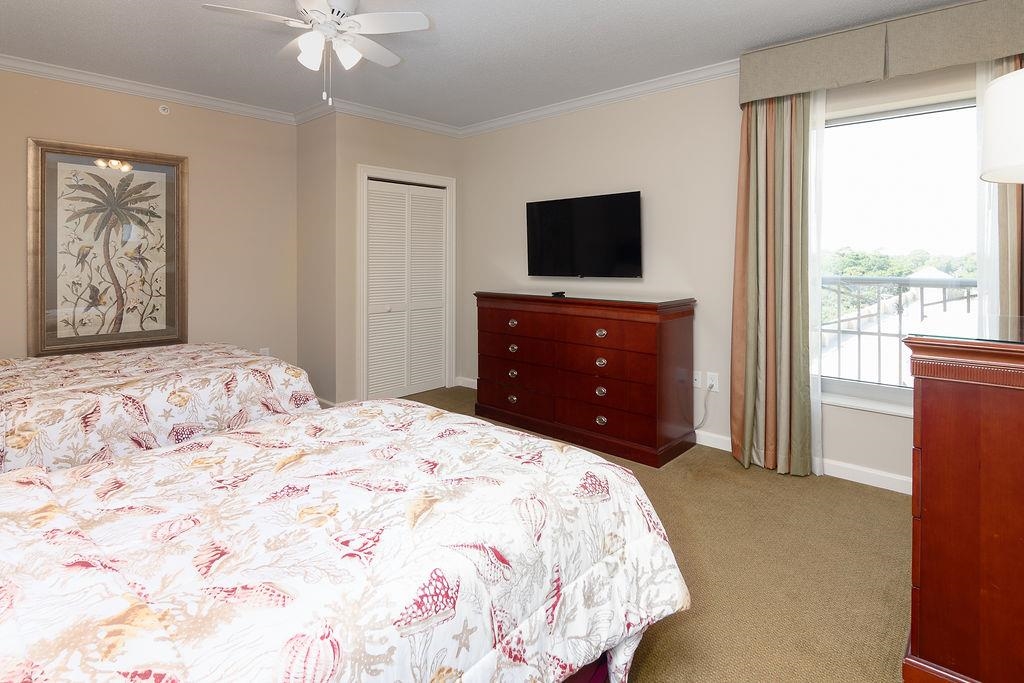 Bedroom with a floral bedspread, wooden dresser, wall-mounted TV, and bright window.