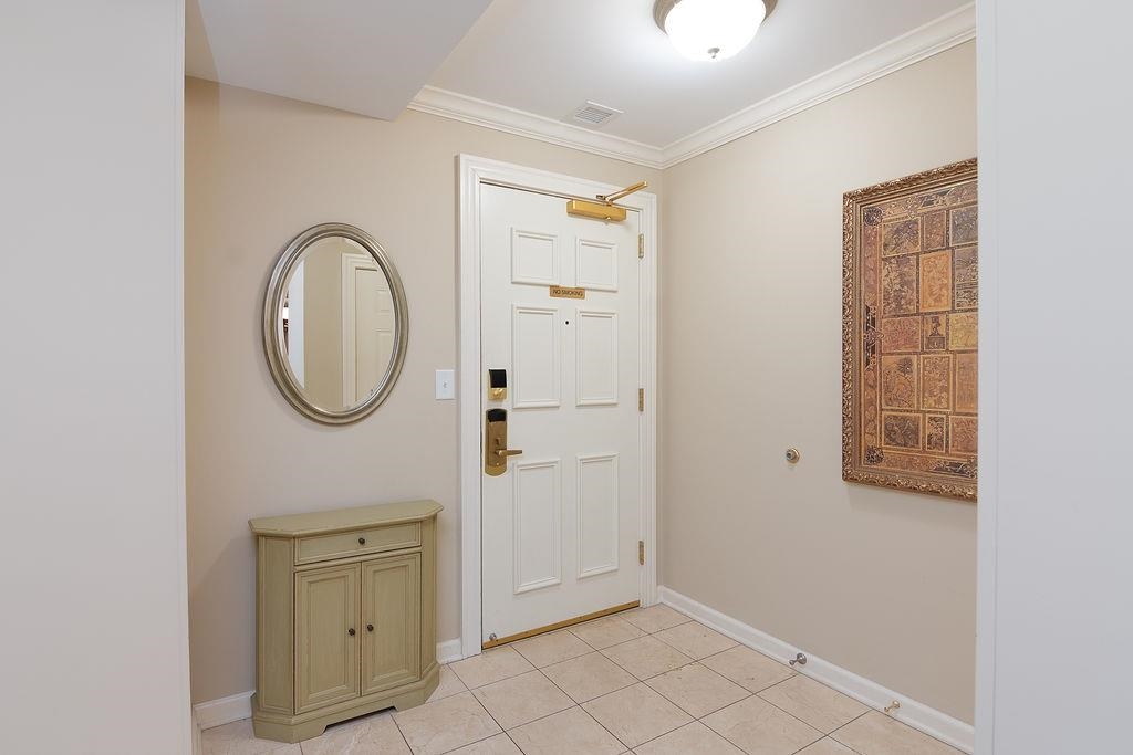 Condo entryway with a white paneled door, tiled floor, oval mirror, and small cabinet.