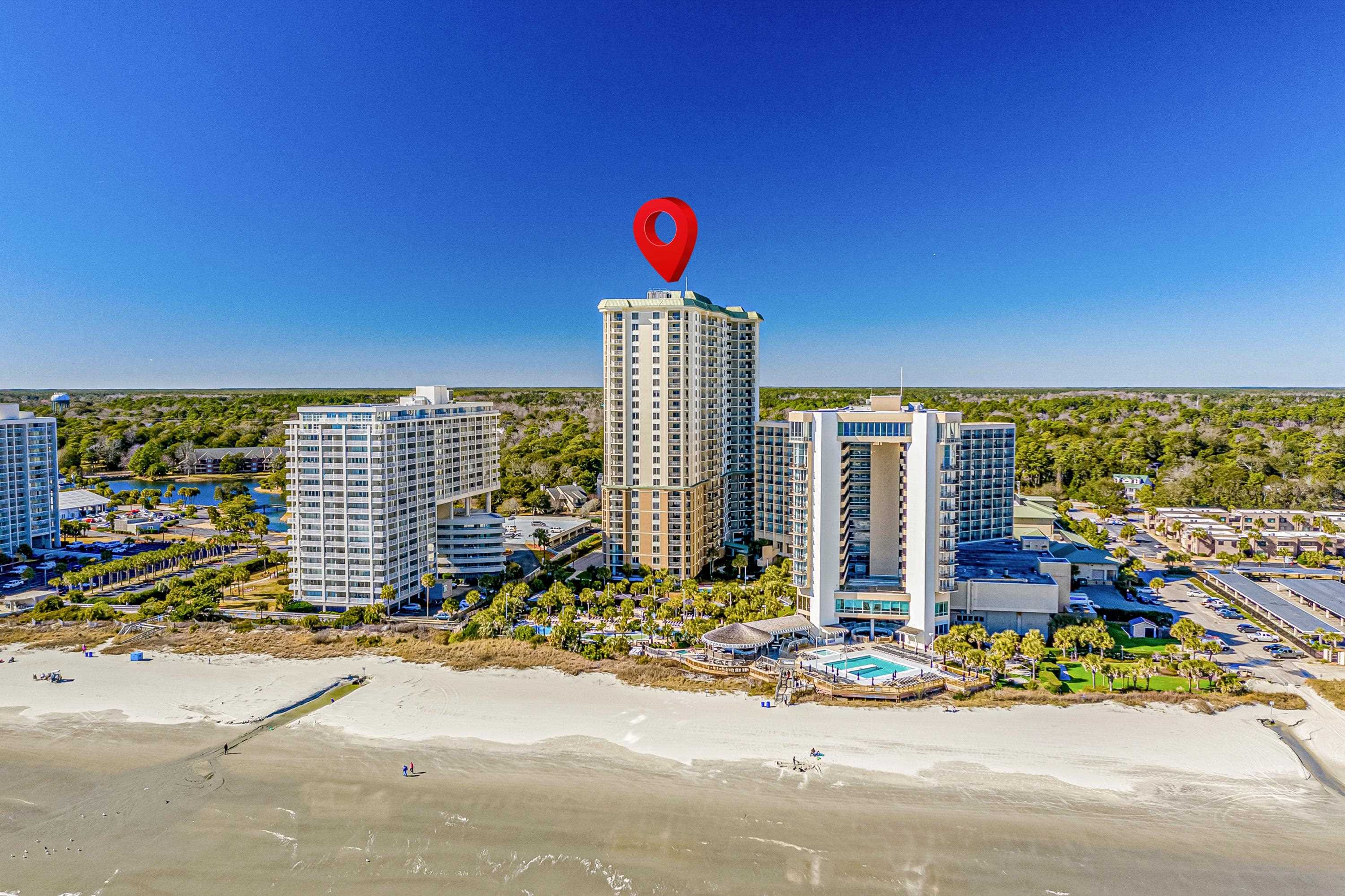Beachfront condominium towers beside a sandy shore, with a red marker above the central high-rise.