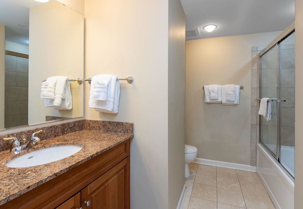 Bathroom with a granite vanity, wood cabinetry, and a glass-enclosed tub and shower.