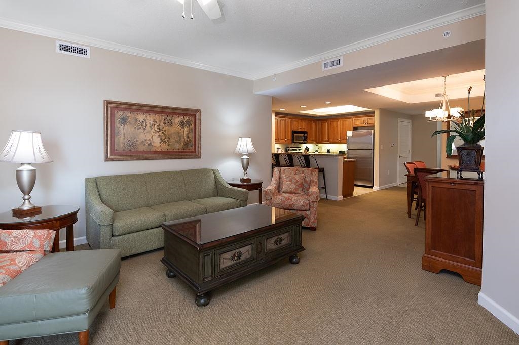 Furnished living room with a green sofa and dark wood coffee table, opening to the kitchen.