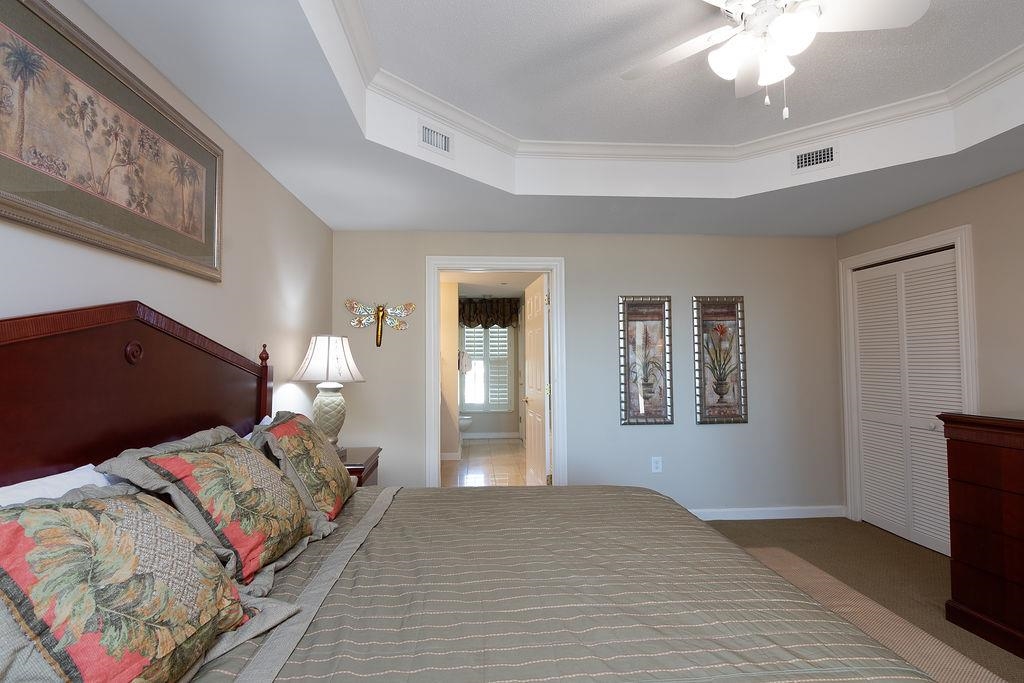 Bedroom with a large bed, tray ceiling, ceiling fan, and doorway to a bright adjoining room.