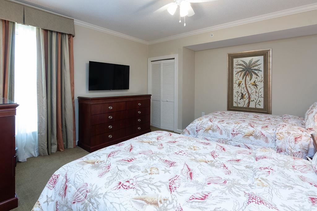 Furnished bedroom with coral-patterned bedding, a dark wood dresser, and framed palm tree artwork.