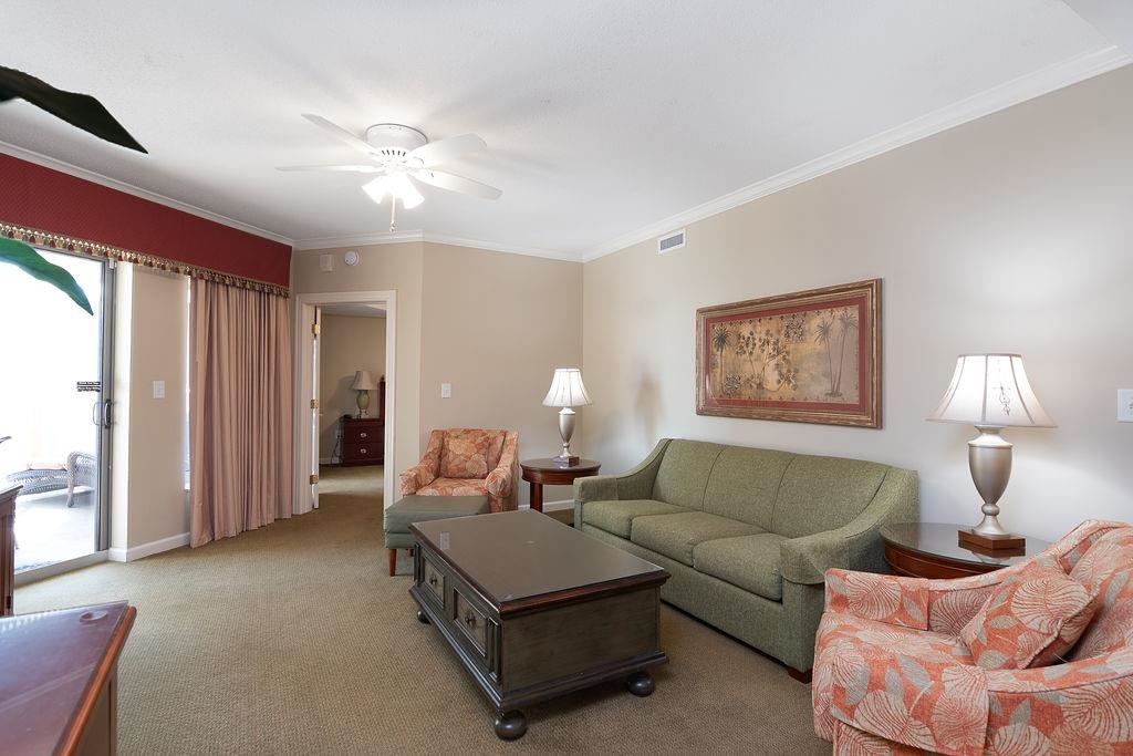 Furnished living room with a green sofa, patterned armchairs, and sliding doors to a balcony.