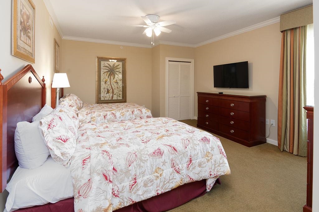 Bedroom with two floral-covered beds, a ceiling fan, and a wall-mounted TV.