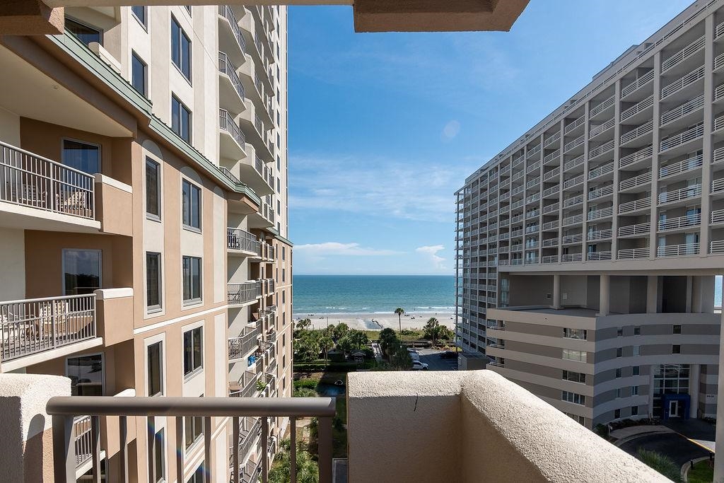 Condominium balcony overlooking the beach and ocean between two high-rise buildings.