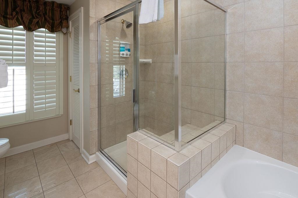 Bathroom with a glass-enclosed tiled shower, built-in tub, and plantation-shuttered window.