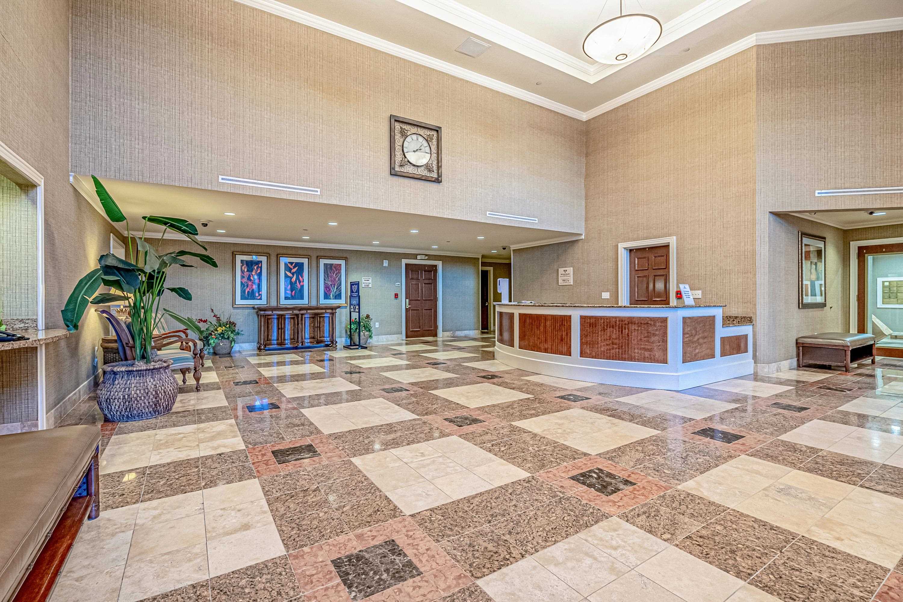 Condominium lobby with a curved reception desk, patterned stone flooring, and a large potted plant.