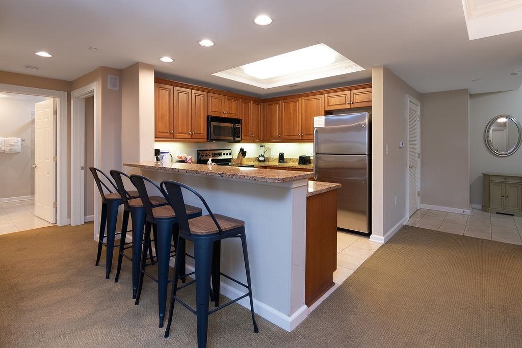 Kitchen with wood cabinetry, stainless steel appliances, and a granite breakfast bar with three stools.