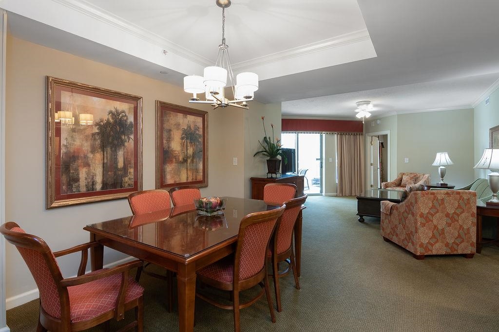 Dining area with a polished wood table and red chairs opens to a carpeted living room.
