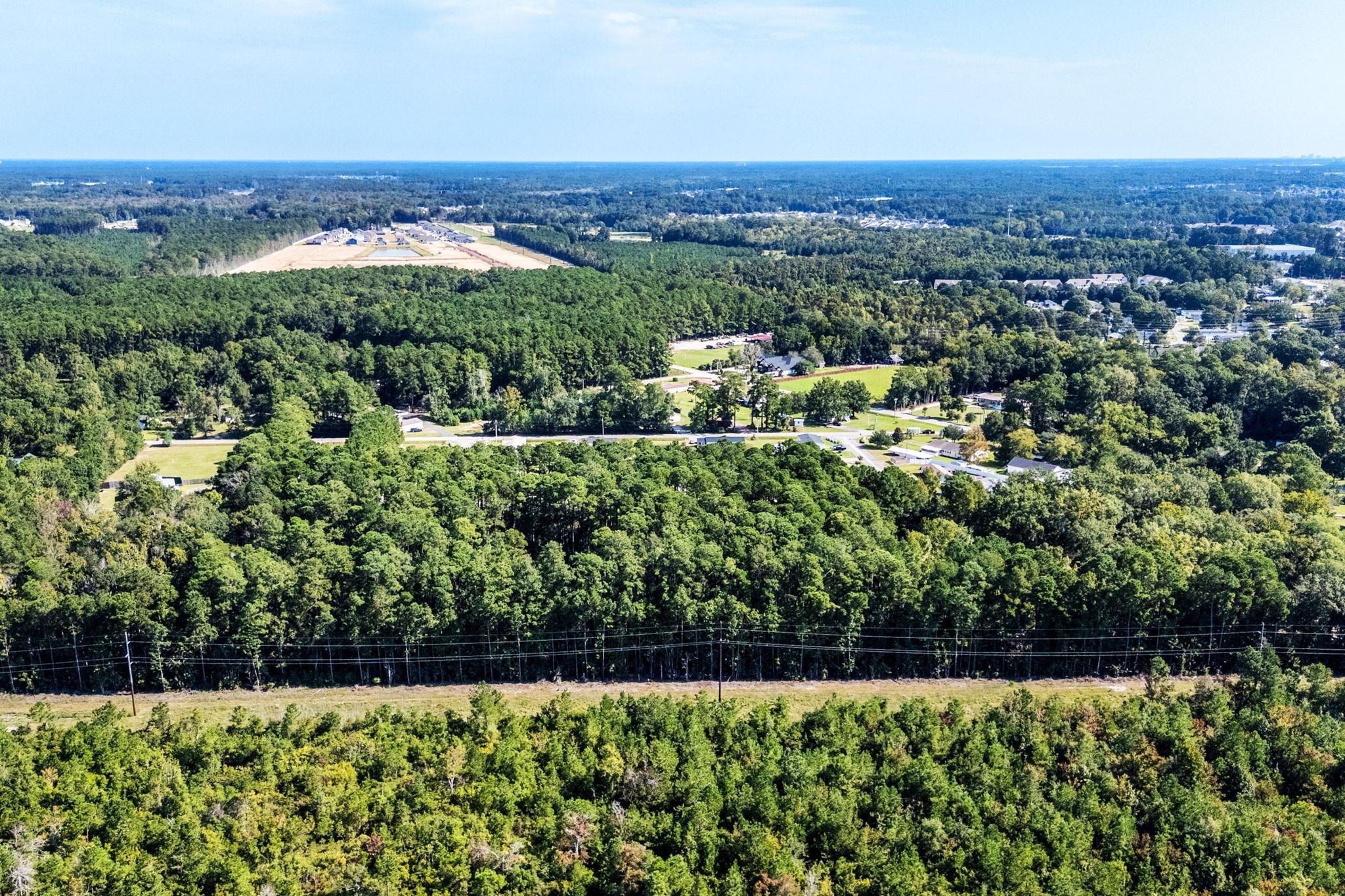 Aerial view of wooded land with utility lines, nearby homes, and roads.