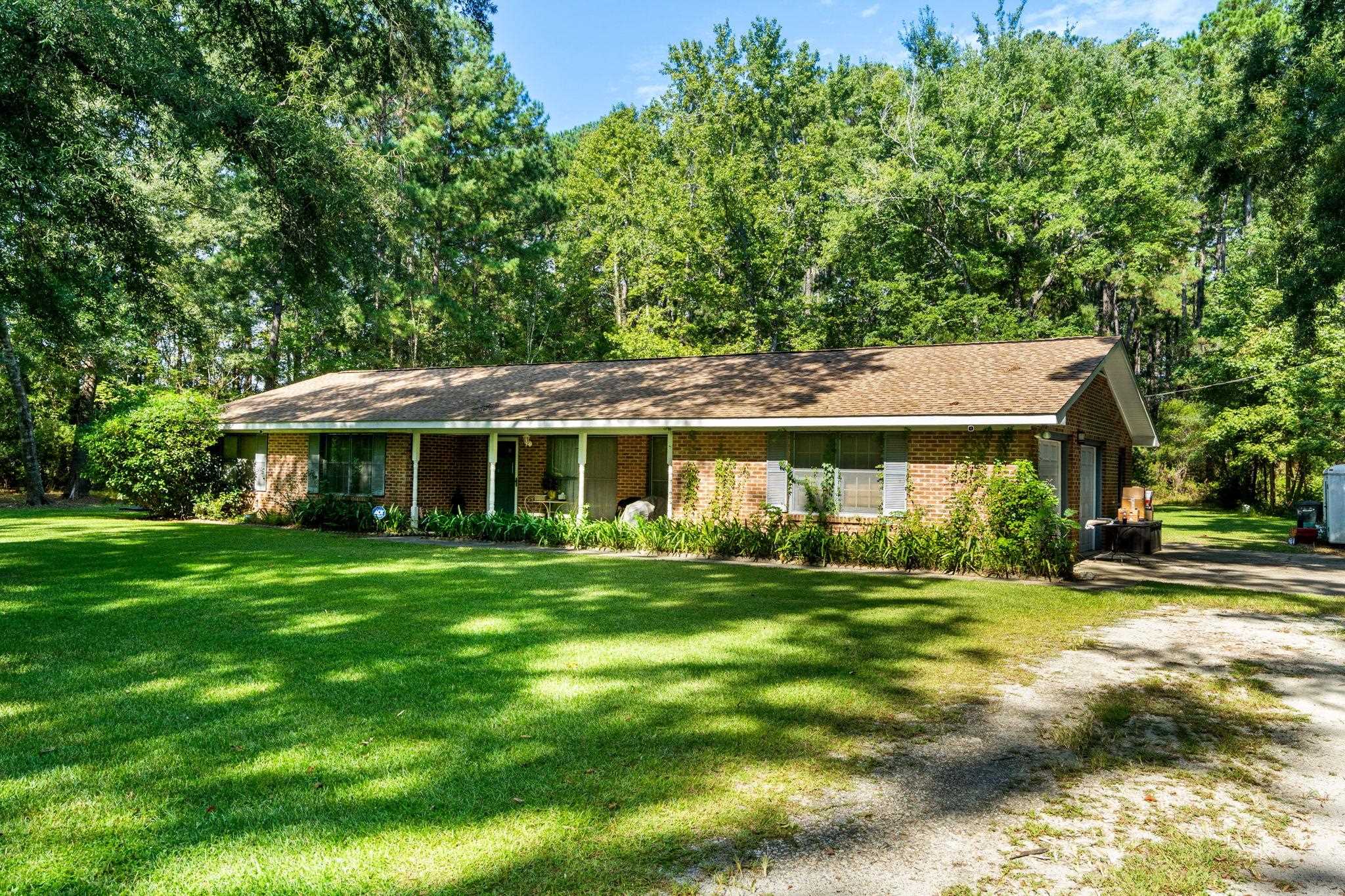 Single-story brick ranch with a covered porch, broad lawn, and mature trees.