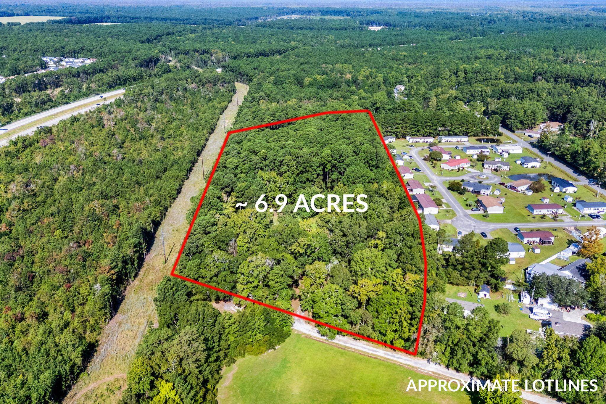 Aerial view of a wooded 6.9-acre parcel outlined in red beside a residential neighborhood.