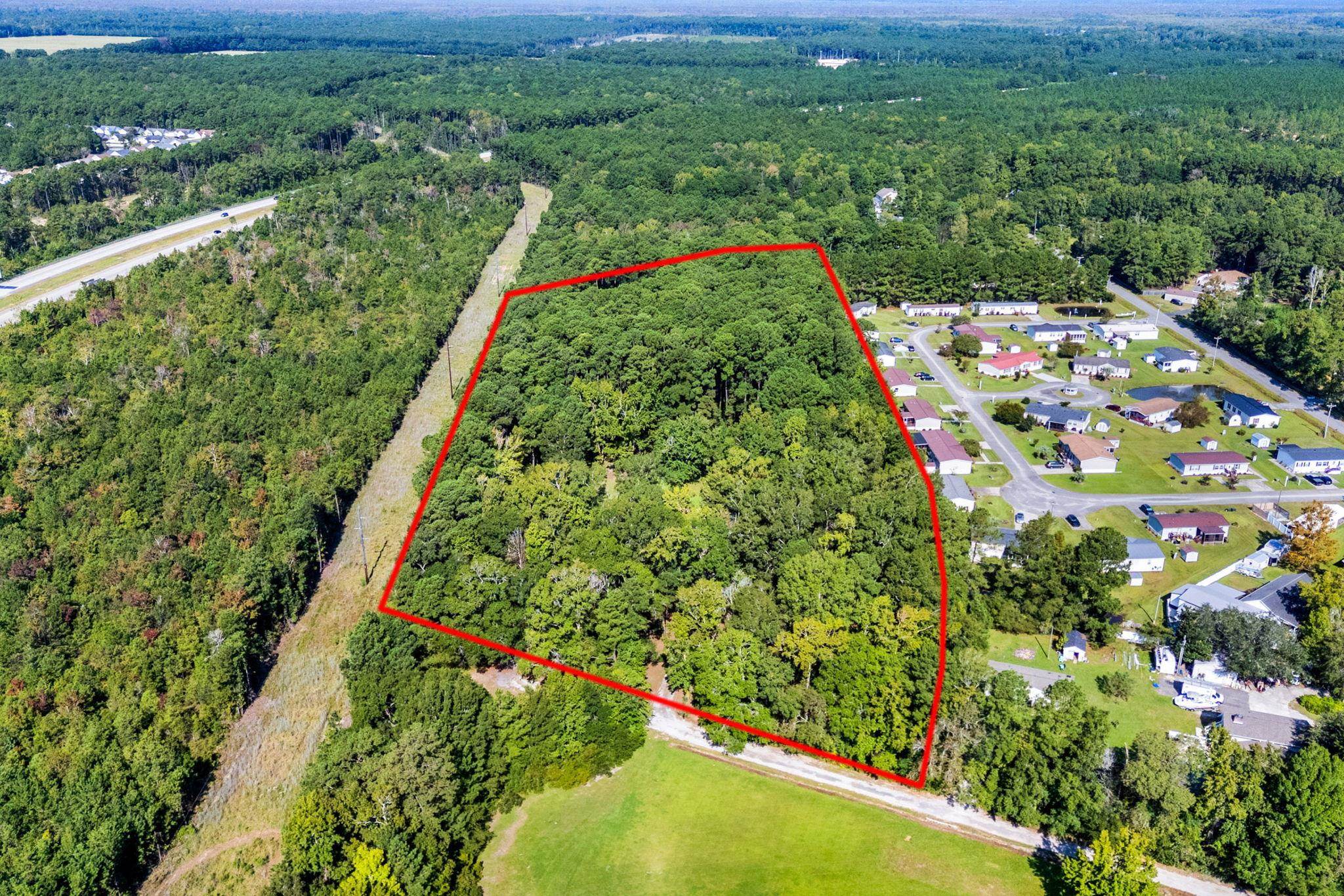 Aerial view of a wooded parcel outlined in red beside a residential neighborhood.