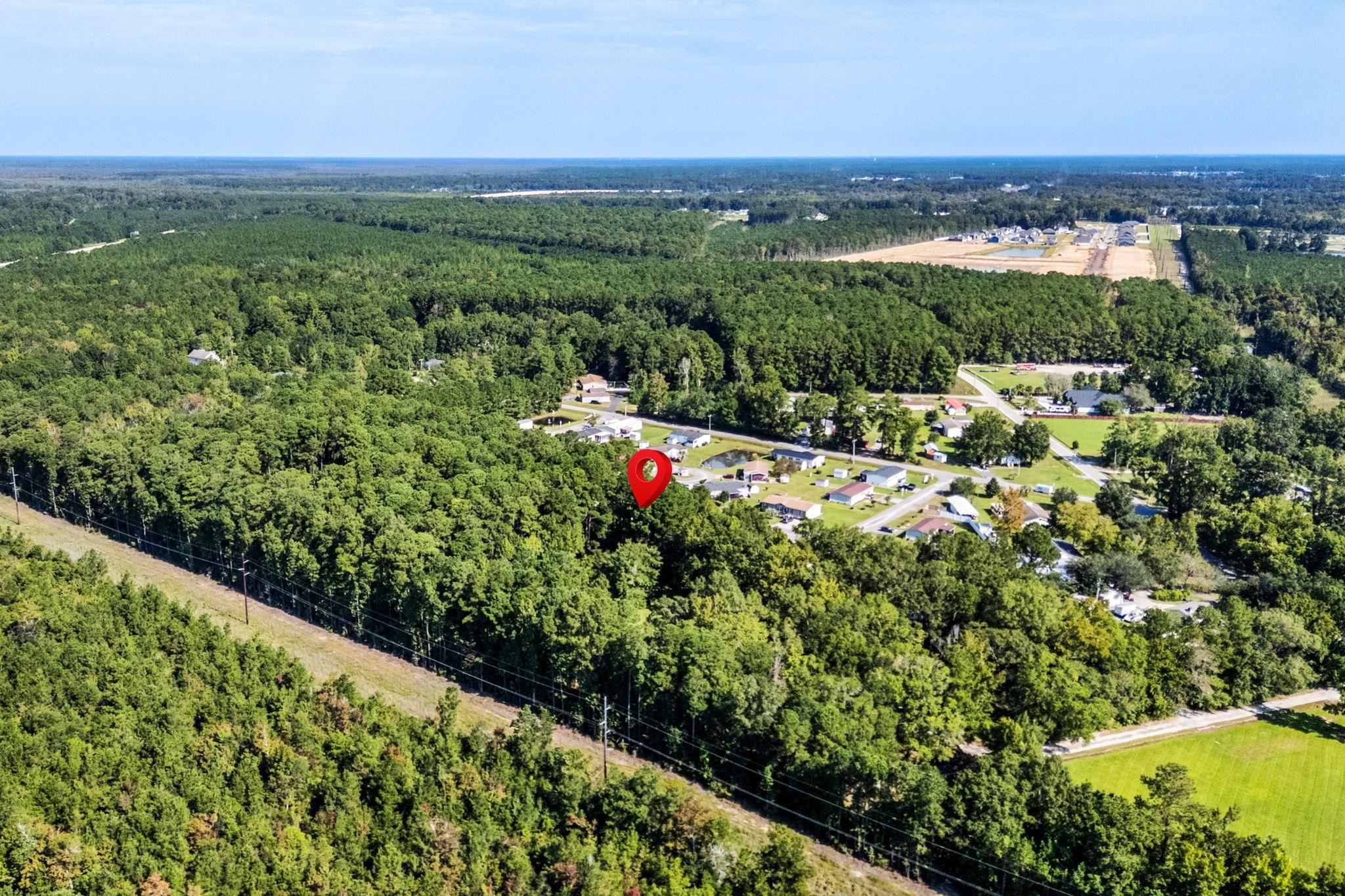 Aerial view of wooded land marked by a red pin near homes and a power line corridor.