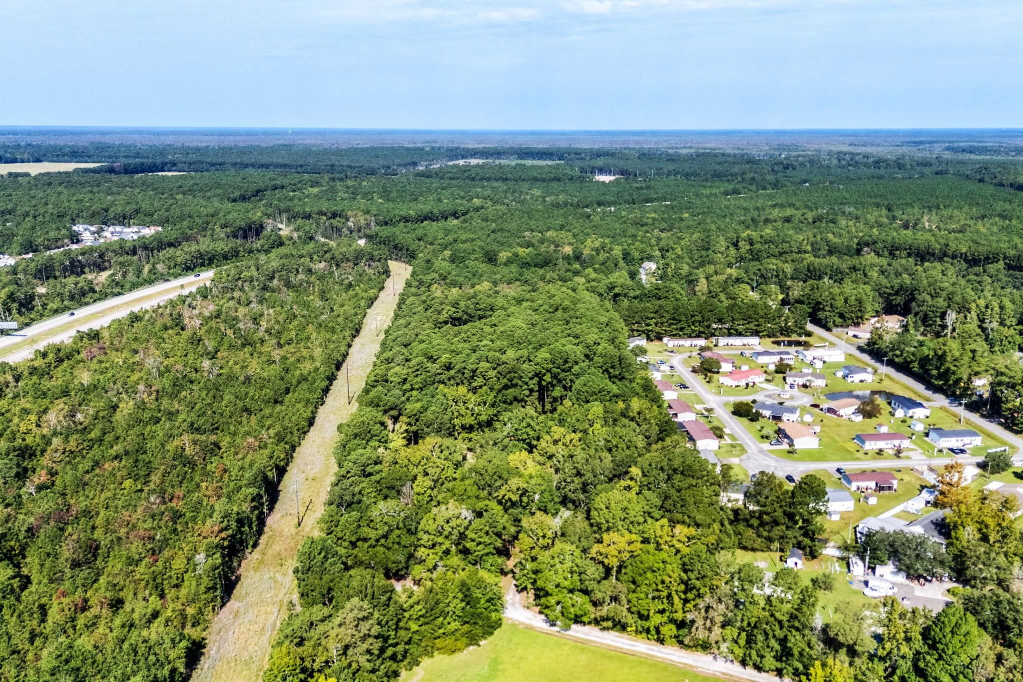 Aerial view of wooded land beside a residential neighborhood and highway.