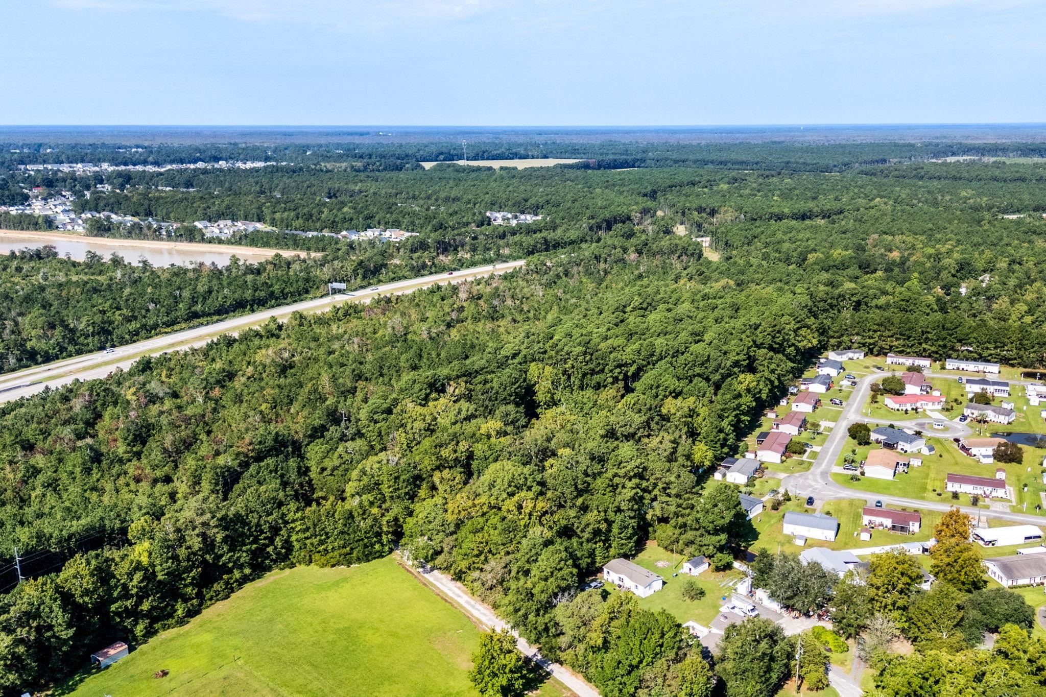 Aerial view of wooded land and an open grassy parcel beside a neighborhood and highway.
