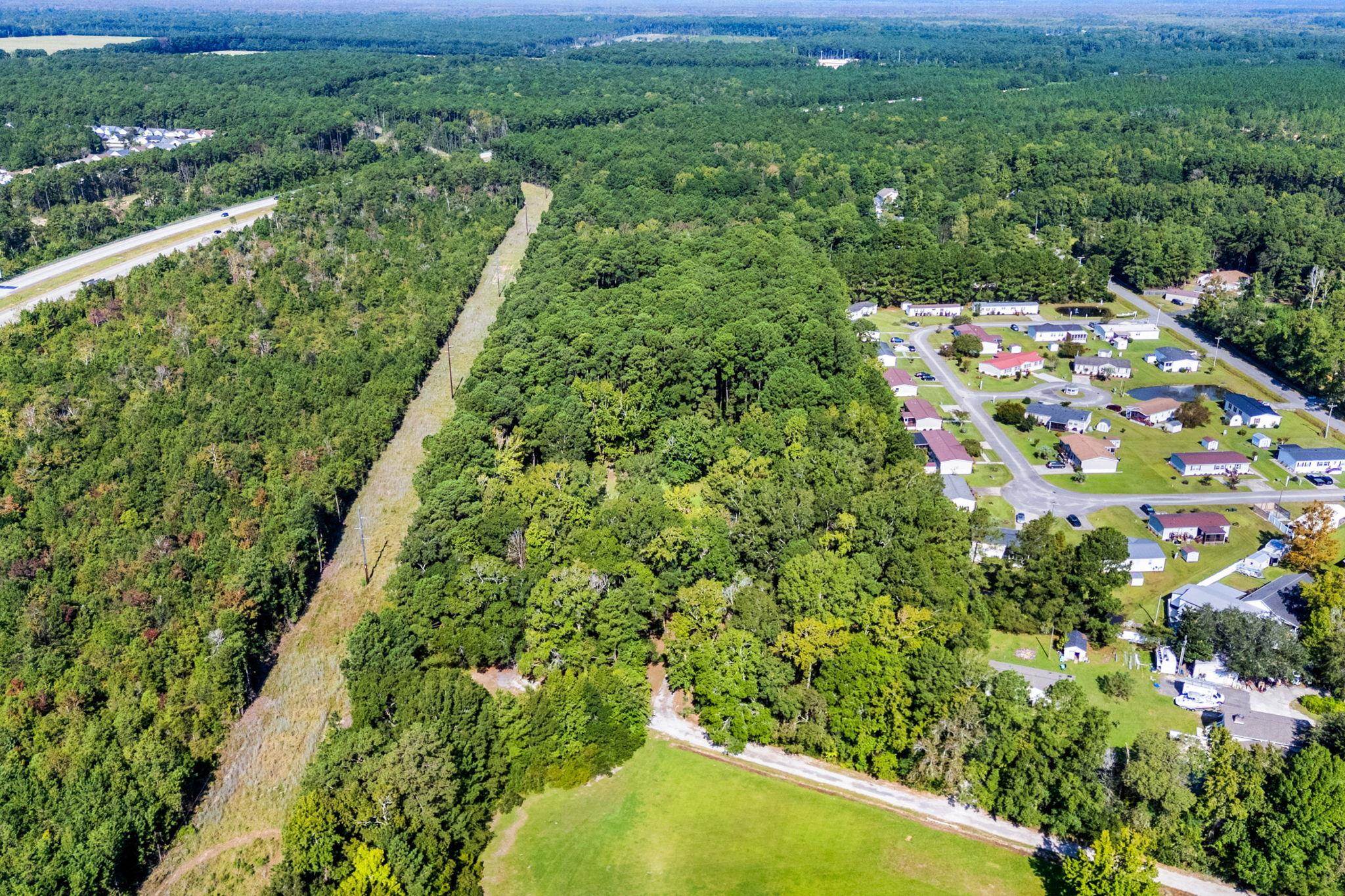 Aerial view of wooded land beside a residential neighborhood, with a grassy clearing and highway nearby.