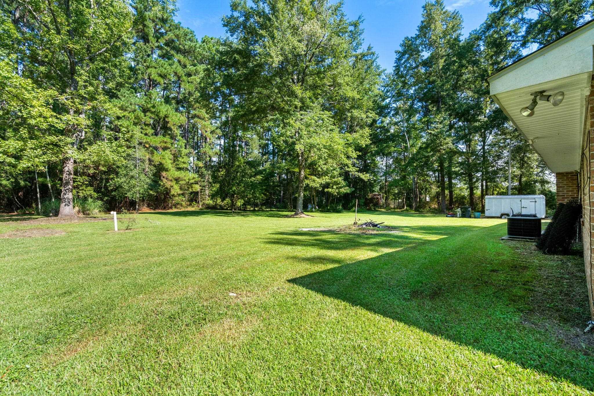 Spacious grassy backyard bordered by mature trees, viewed beside the house.