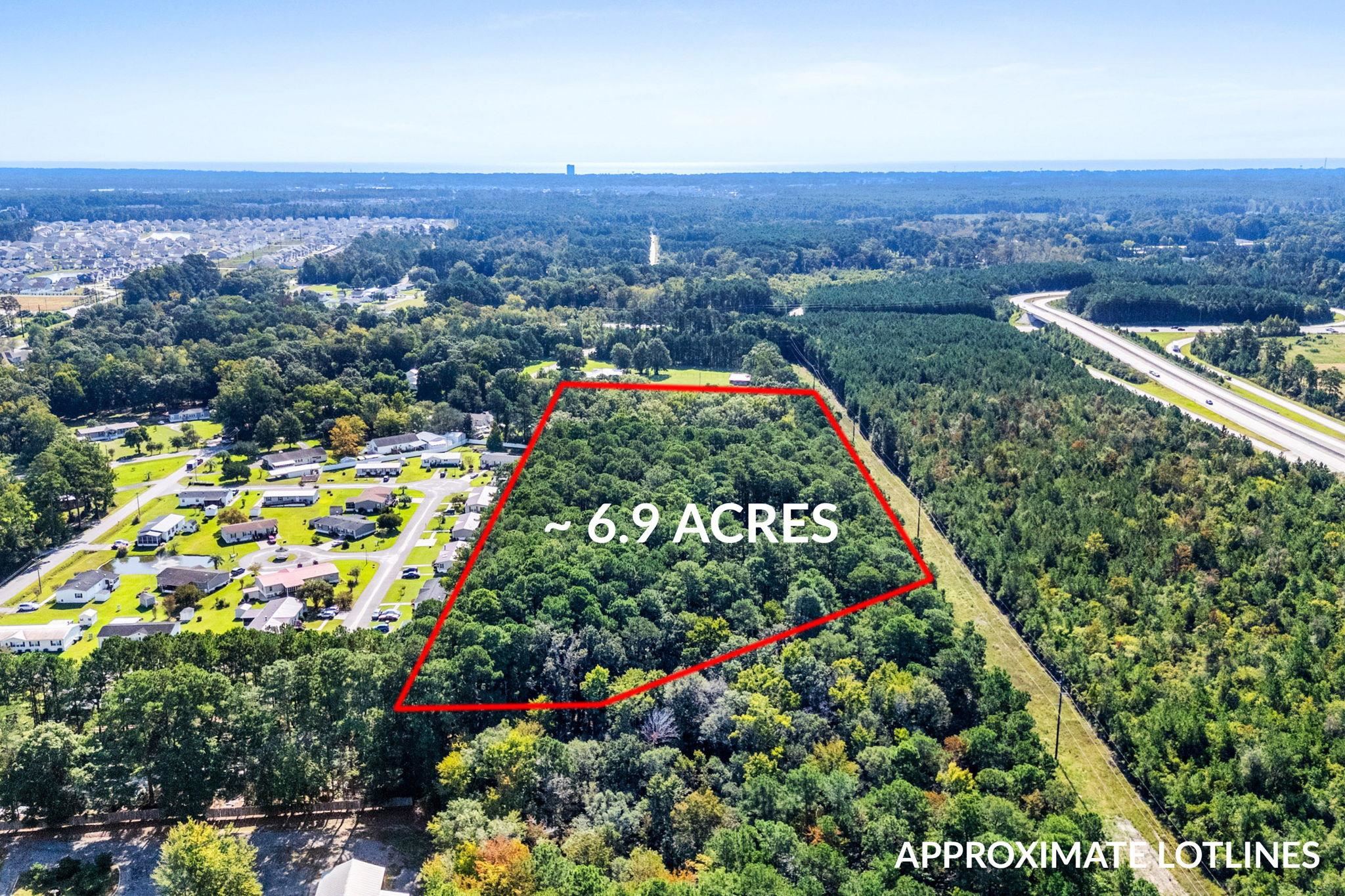 Aerial view of wooded 6.9-acre parcel outlined in red beside a residential neighborhood and highway.