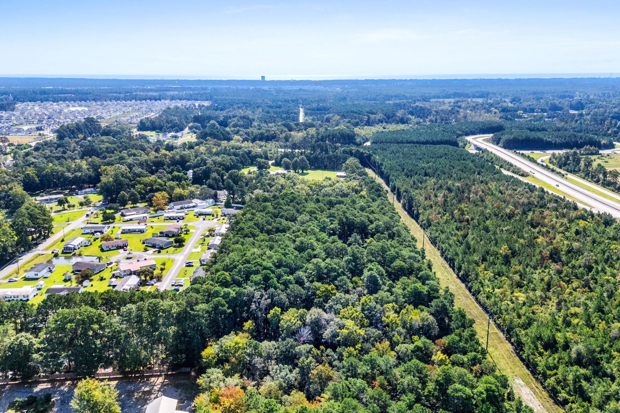 Aerial view of dense wooded land beside homes and a curving divided highway.