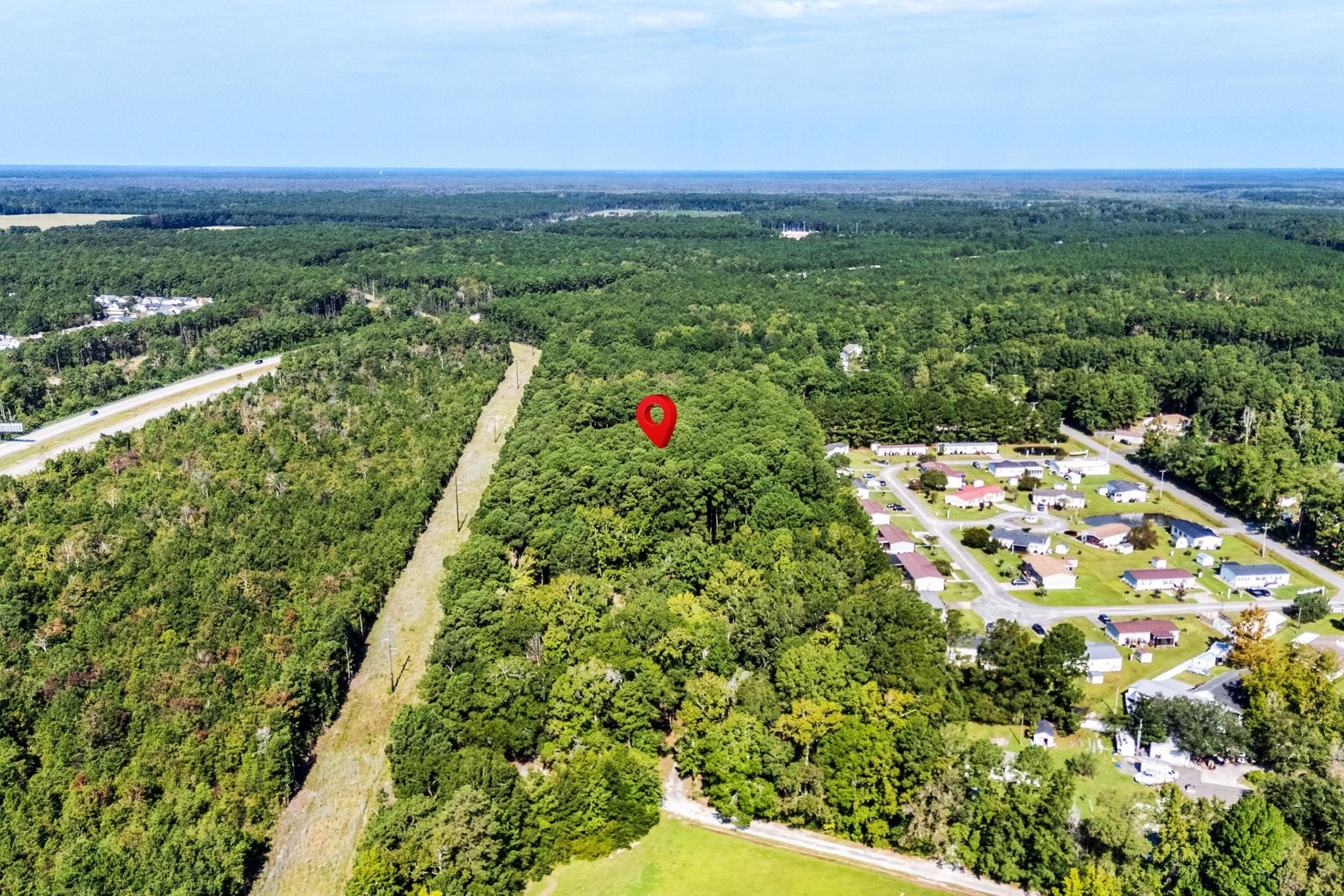 Aerial view of a wooded vacant parcel marked by a red pin, with nearby homes and a highway.